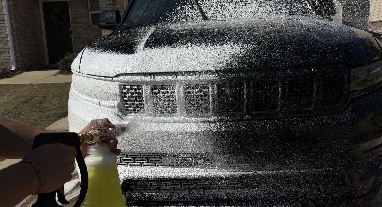 Person using a foam cannon to wash a black SUV.