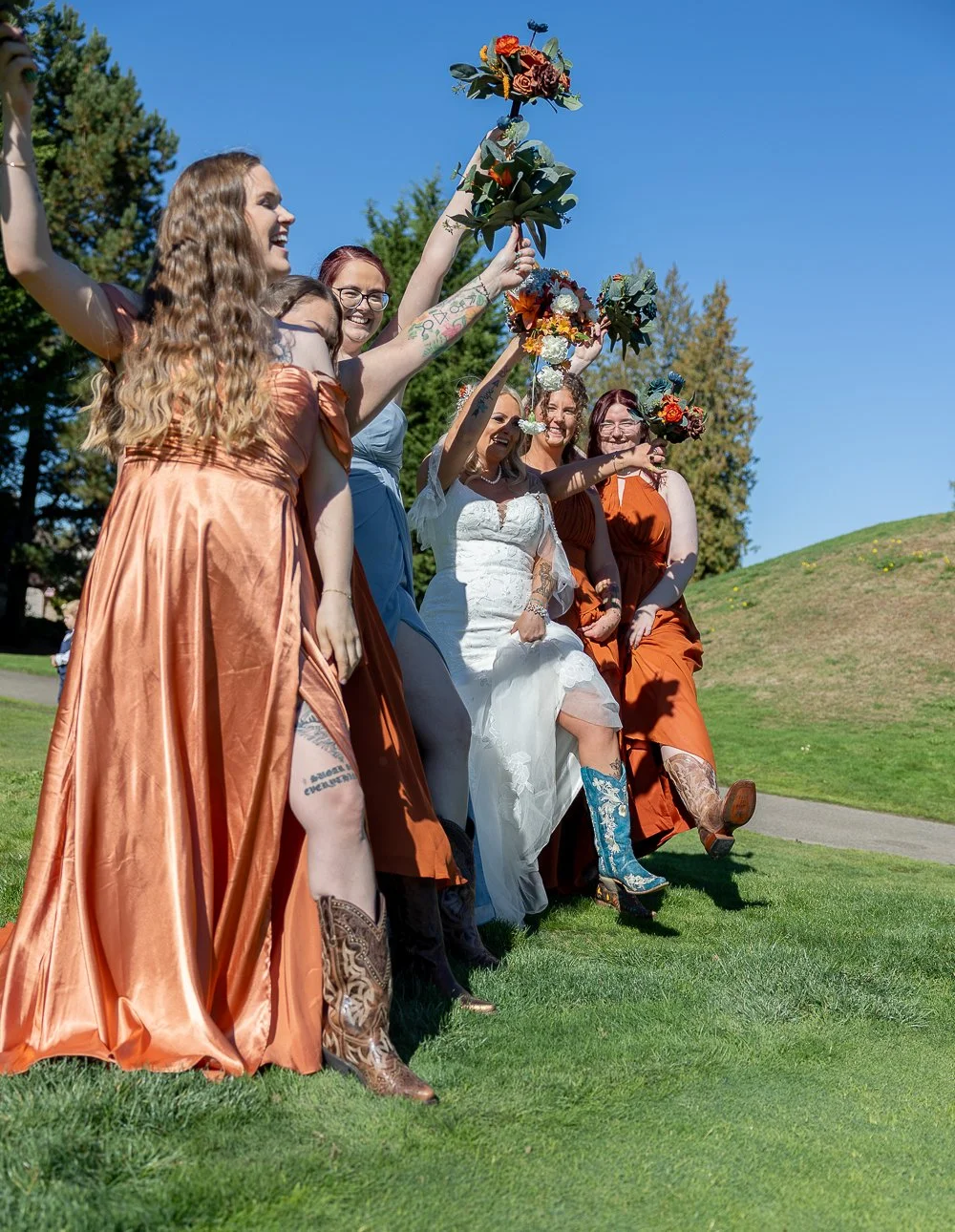 Group of women in colorful dresses celebrating outdoors on a sunny day, holding flowers.