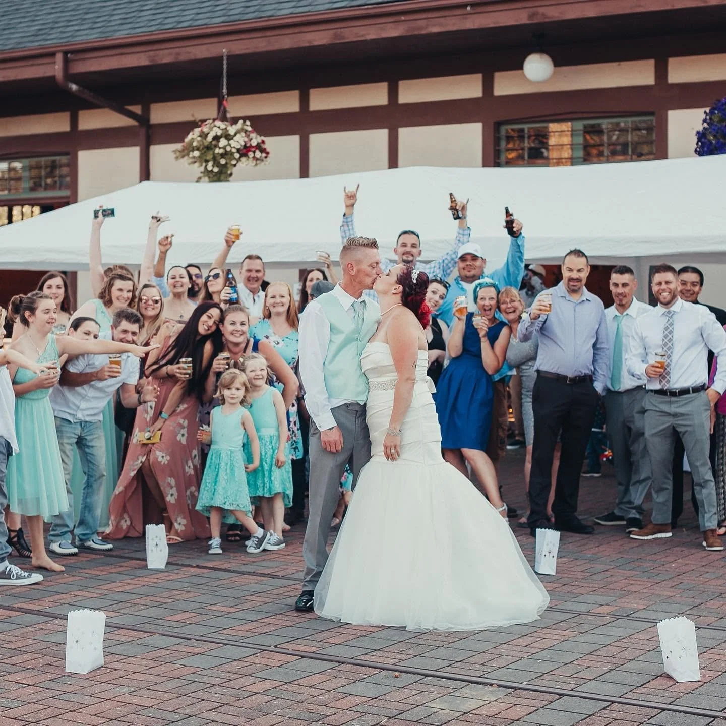 A bride and groom kiss in front of wedding guests at an outdoor celebration.