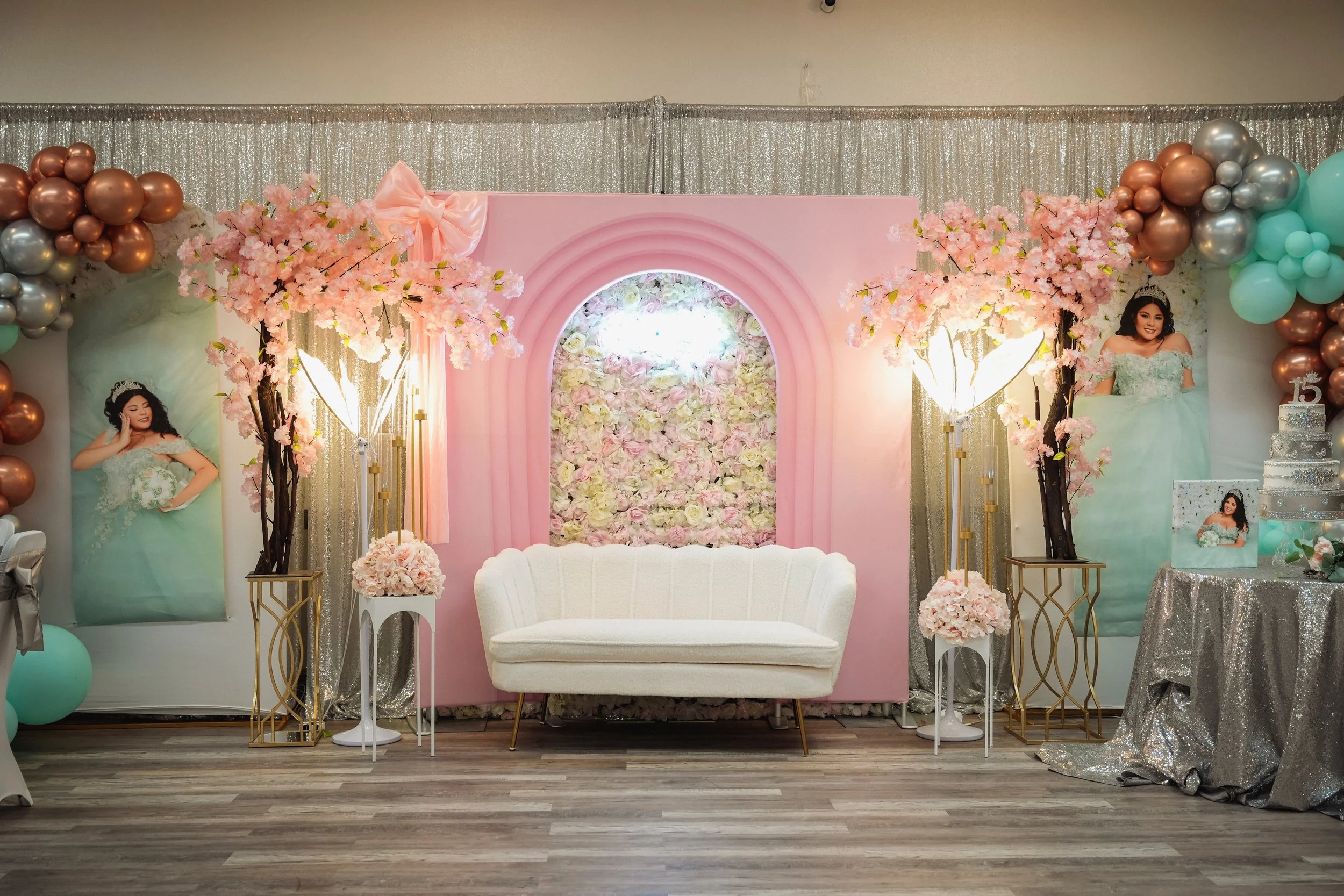 Decorative backdrop with pink, gold, and silver accents, including balloons, cherry blossom branches, and floral designs for a celebration or party.