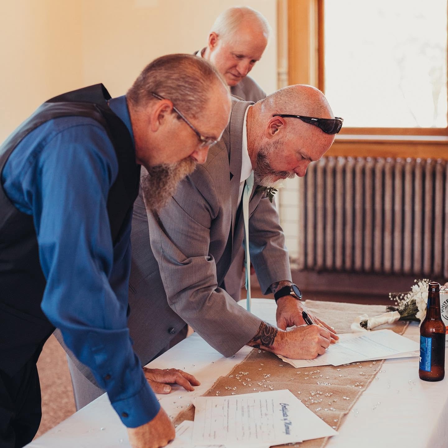 Three men in formal attire signing documents at a table during a ceremony