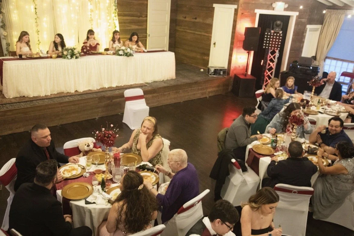 Kids' table with girls in fancy dresses and adults' tables with people eating and talking at a festive event.