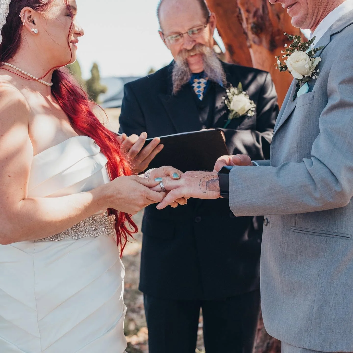 A couple getting married, exchanging rings outdoors, with officiant present.
