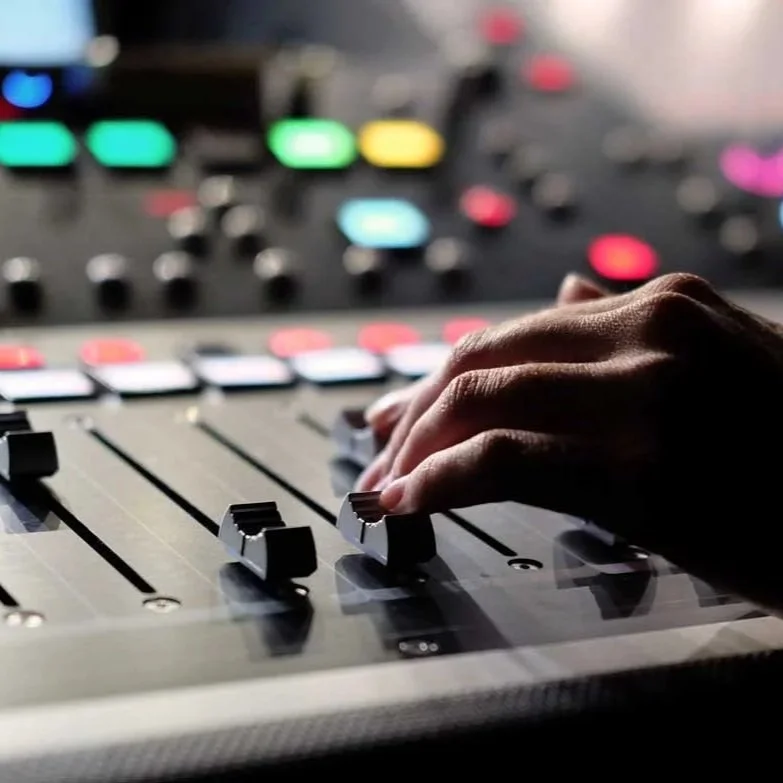 Close-up of a hand adjusting a knob on a professional audio mixing console with colorful LED displays in the background.