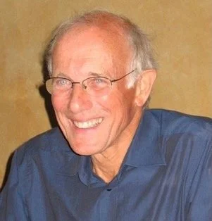 A smiling elderly man with glasses, wearing a blue shirt.
