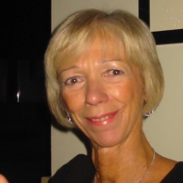A close-up photo of a middle-aged woman with short blonde hair, smiling, wearing earrings and a black top.