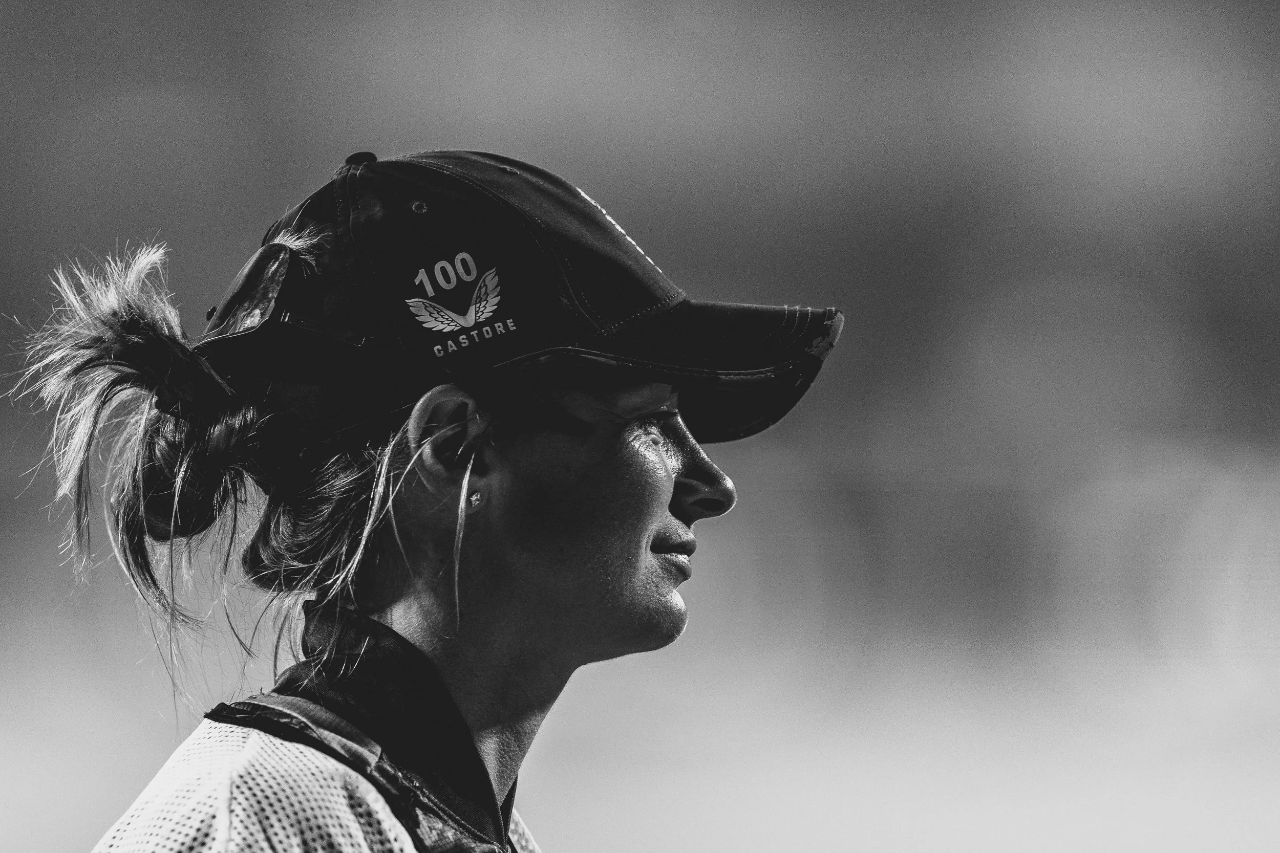 Black and white photo of a female athlete wearing a cap with a logo, standing outdoors against a plain sky background.