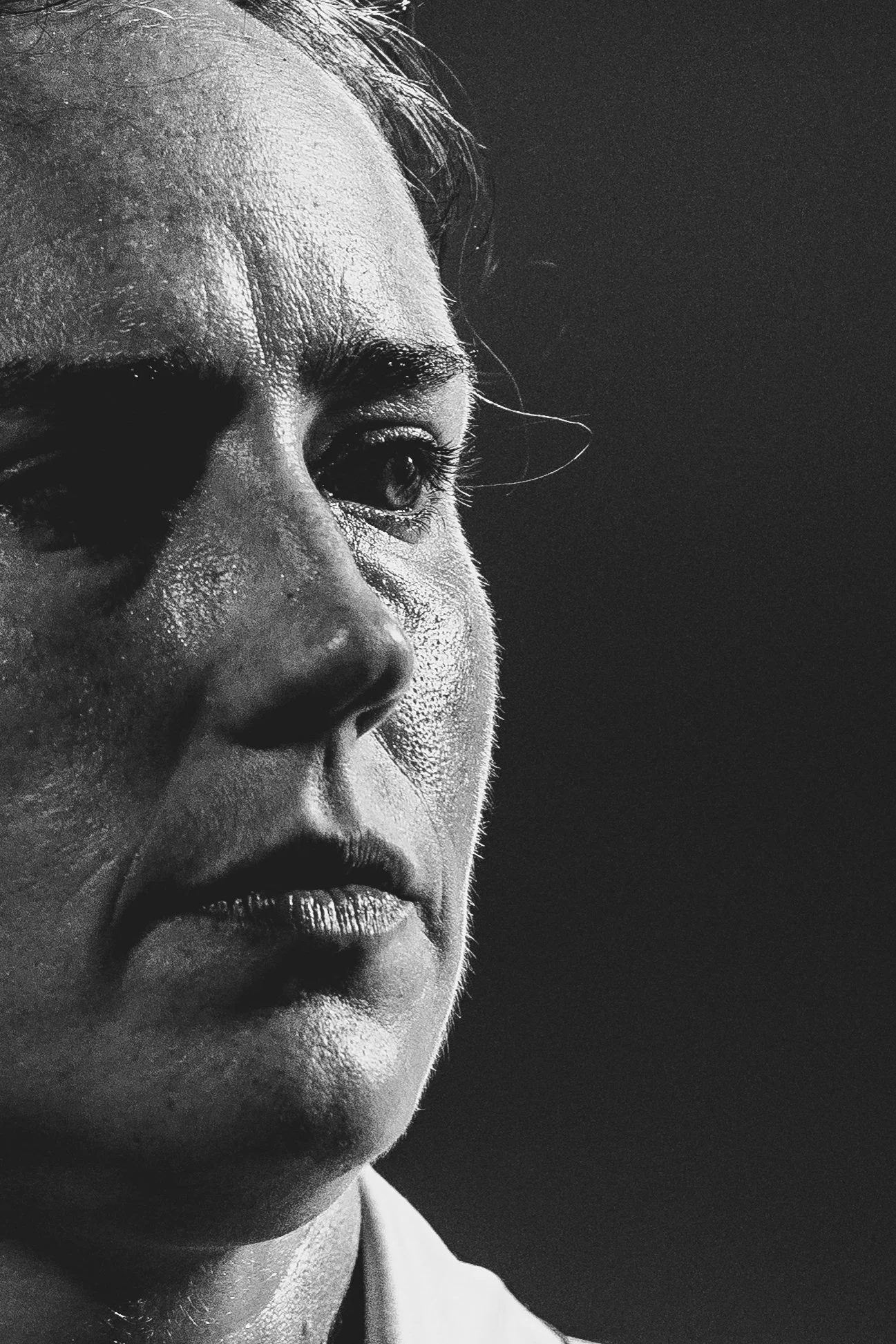 Close-up black and white photo of a woman's face, focusing on her eye, nose, and mouth, with detailed skin texture and slightly messy hair on her forehead.