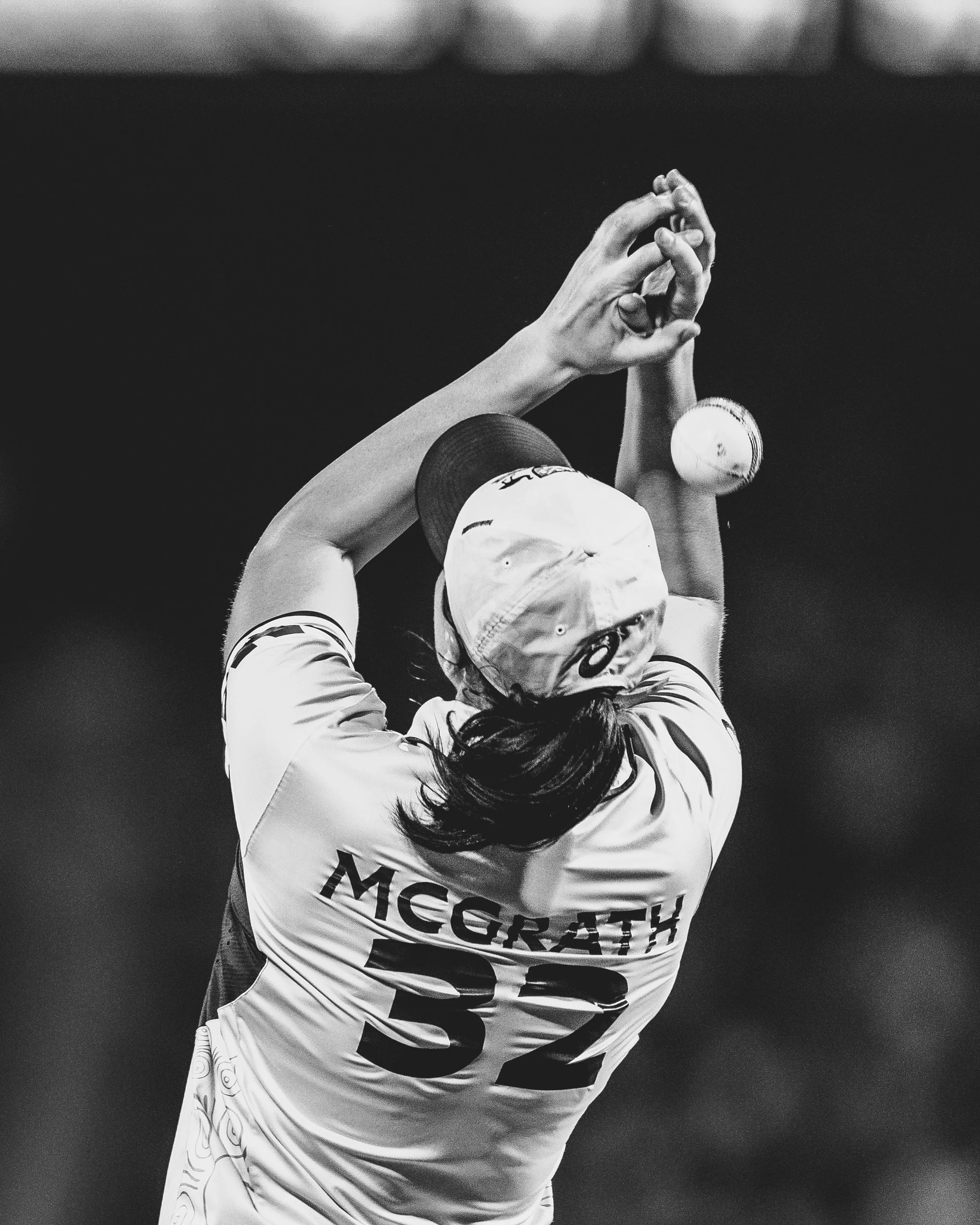 A female tennis player with long hair tied back, wearing a cap, practicing a serve on the court, with her arms raised and hands together preparing to hit the ball.