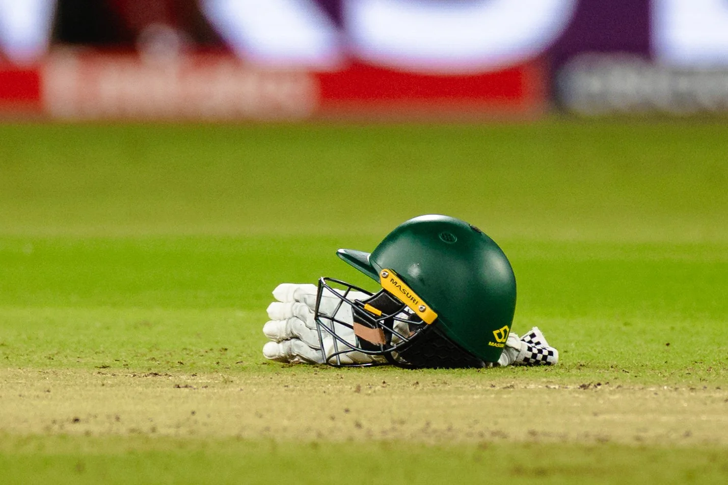 A green cricket helmet, white gloves, and a checkered cloth on a cricket field.