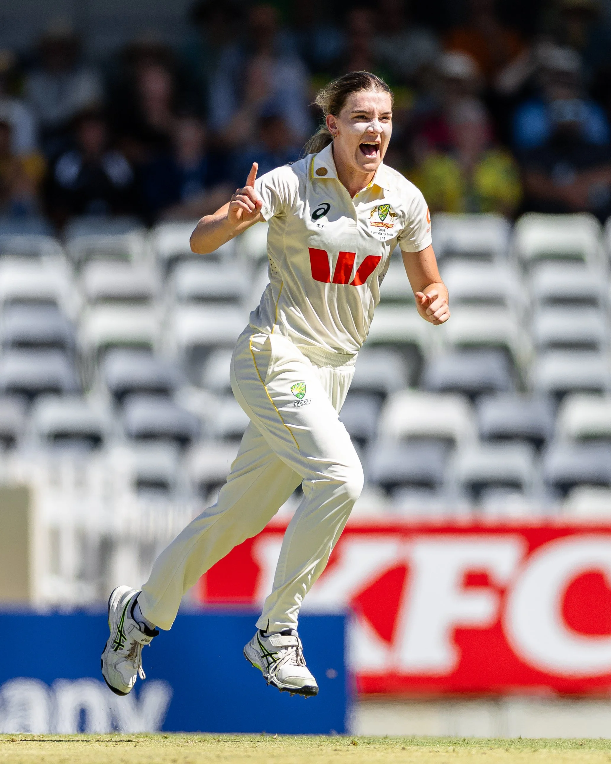 Cricket player in a white uniform celebrating on the field, with a crowd in the background.