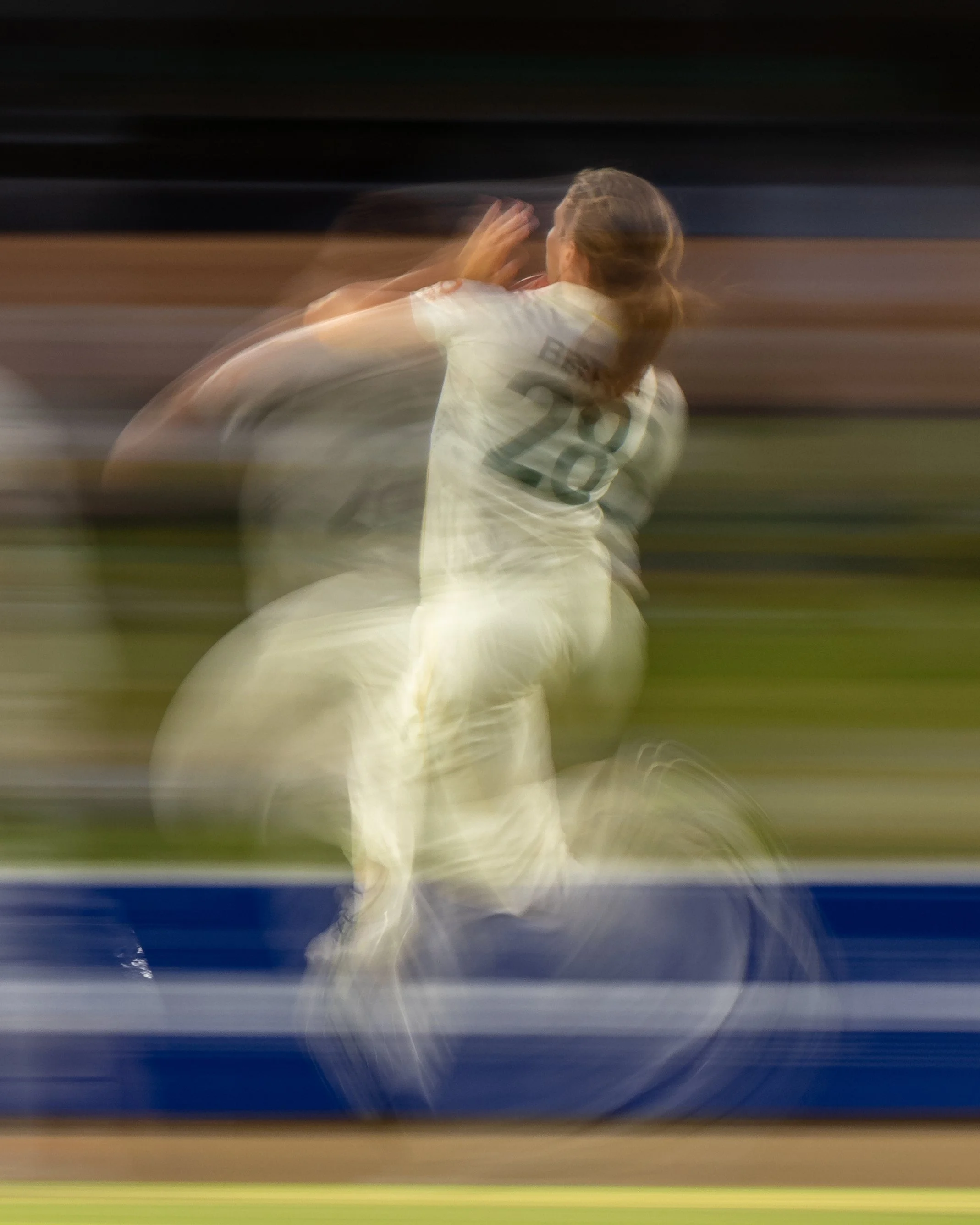 Blurred image of a soccer match, showing a player with jersey number 28 and another player in motion, with stadium lights in the background.