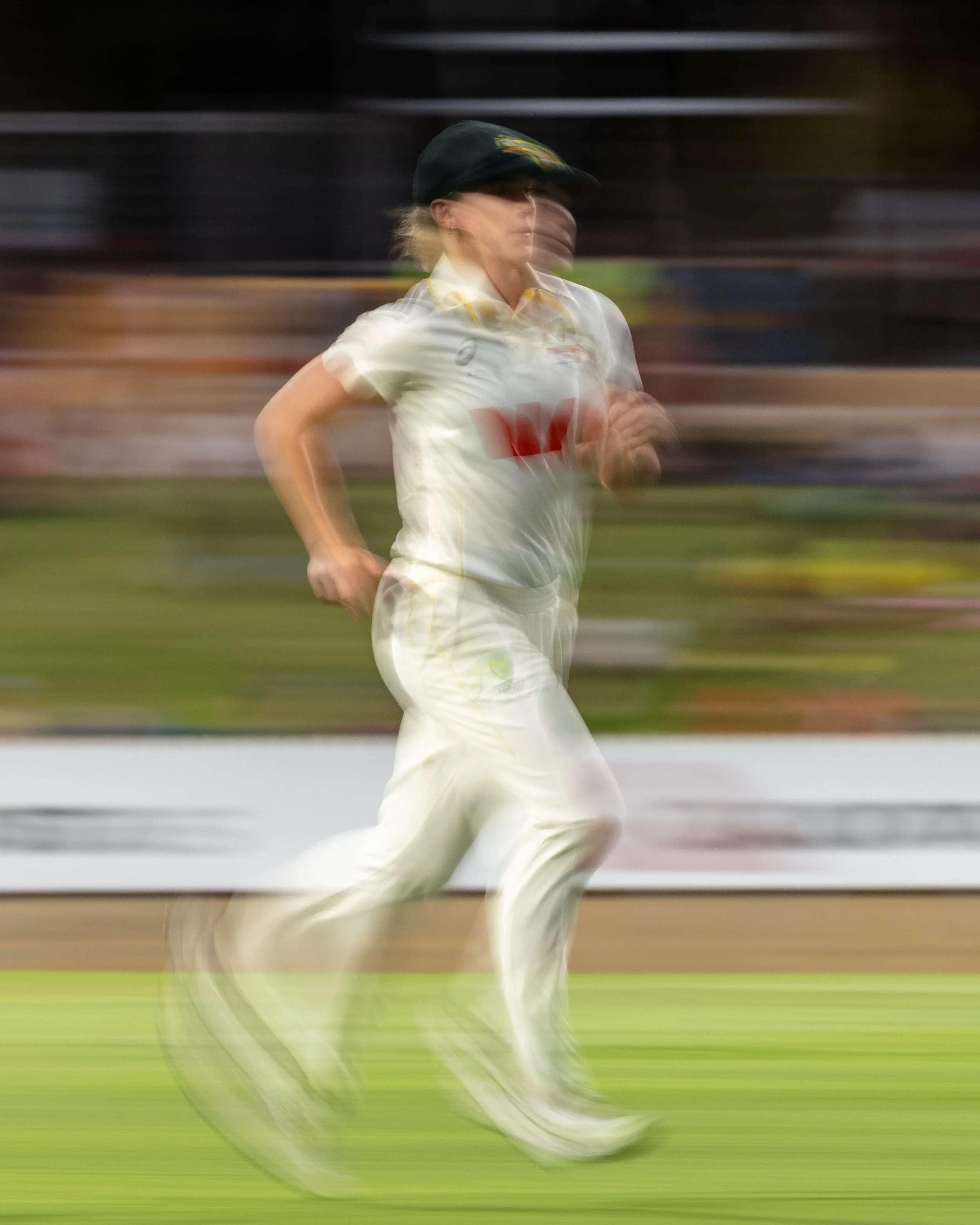Blurred motion image of a woman running on a grassy field at night, wearing a white sports shirt and a cap.