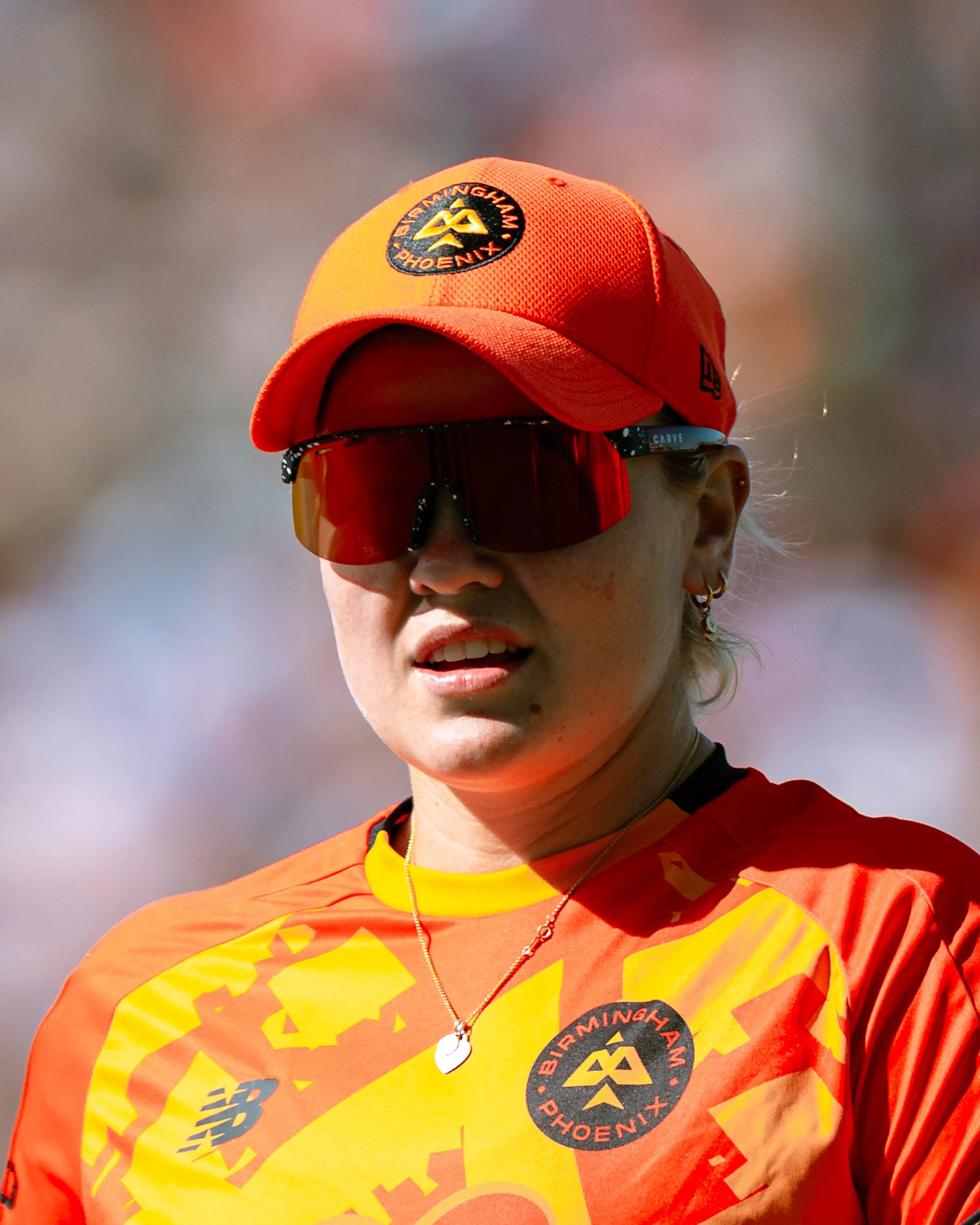 Close-up of a person wearing a red and yellow sports jersey with the Boston Marathon logo, a red cap with the Boston Marathon logo, and sunglasses, outdoors on a sunny day.