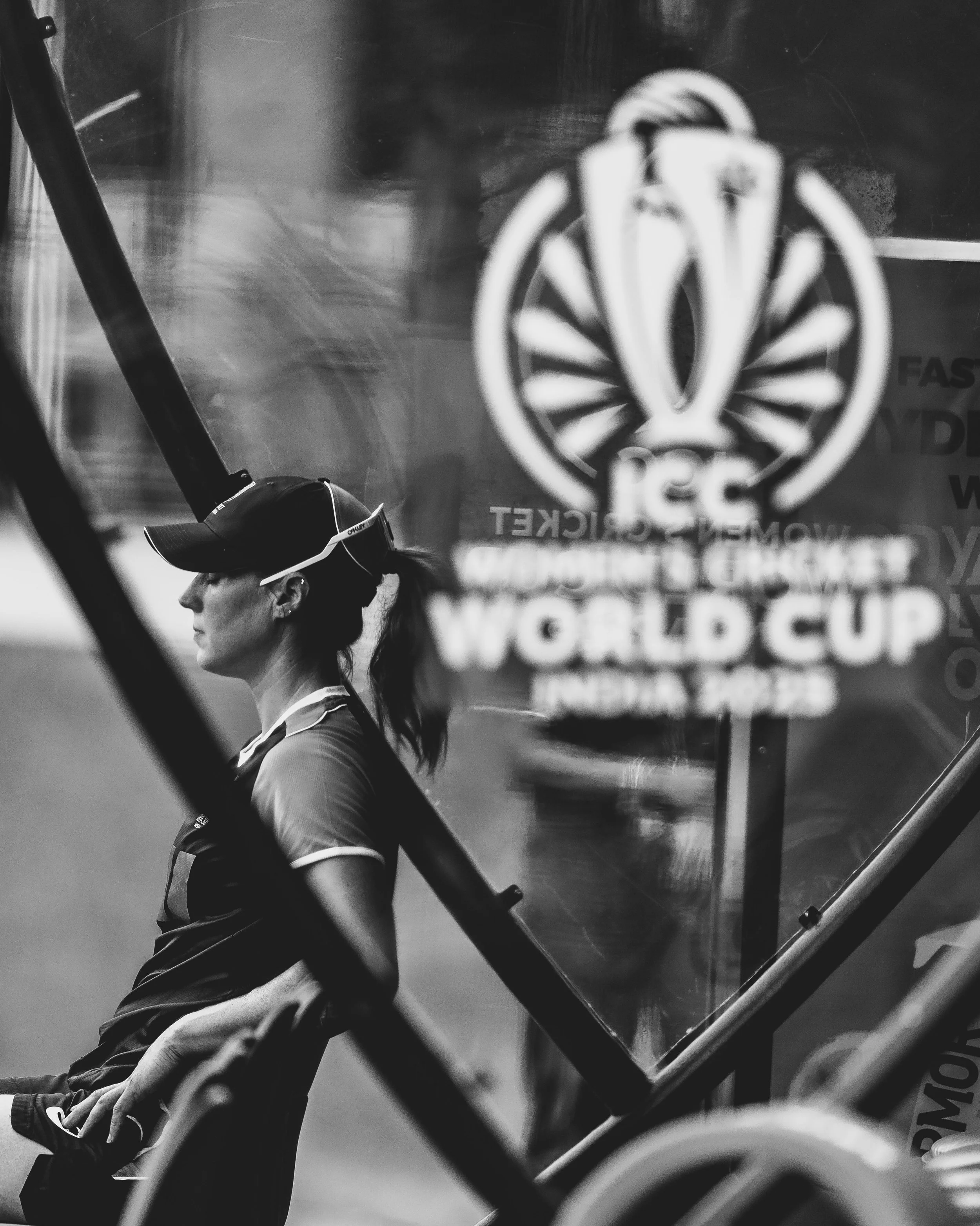 A woman wearing sunglasses and a sports shirt is seen from the side, as viewed through a glass door with an logo that has a wheel design and text, at a gym or fitness center.