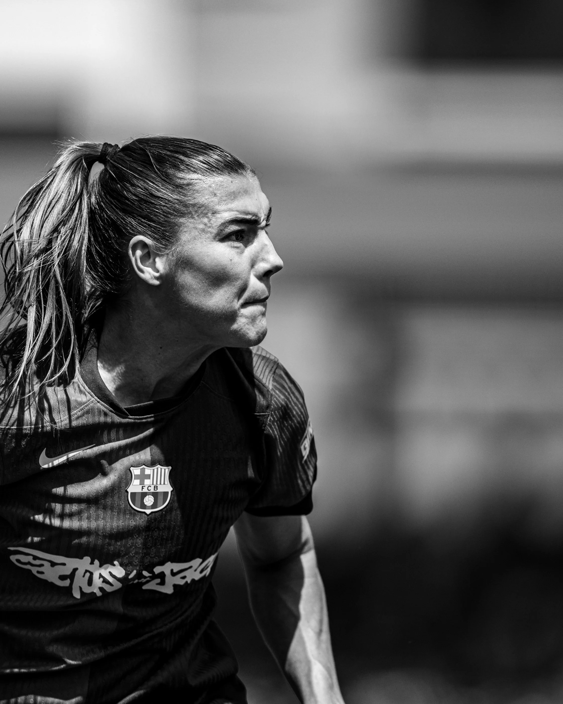 Close-up black and white photo of a male soccer player with a ponytail, wearing a FC Barcelona jersey, focused and looking ahead.