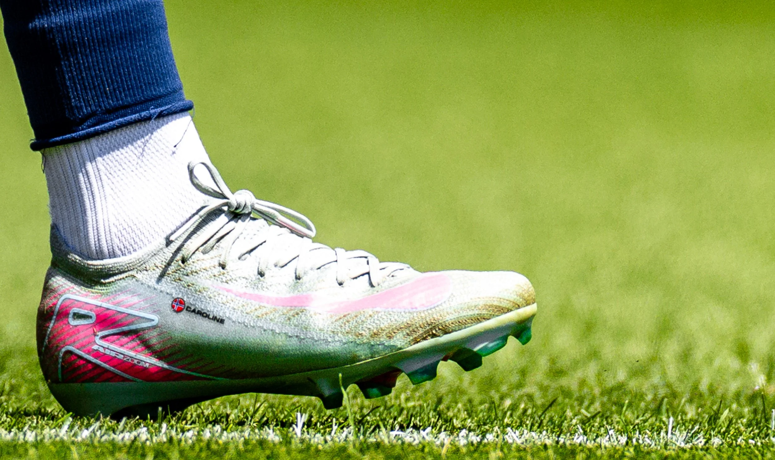Close-up of a person's white and pink sports shoe on a grassy field.