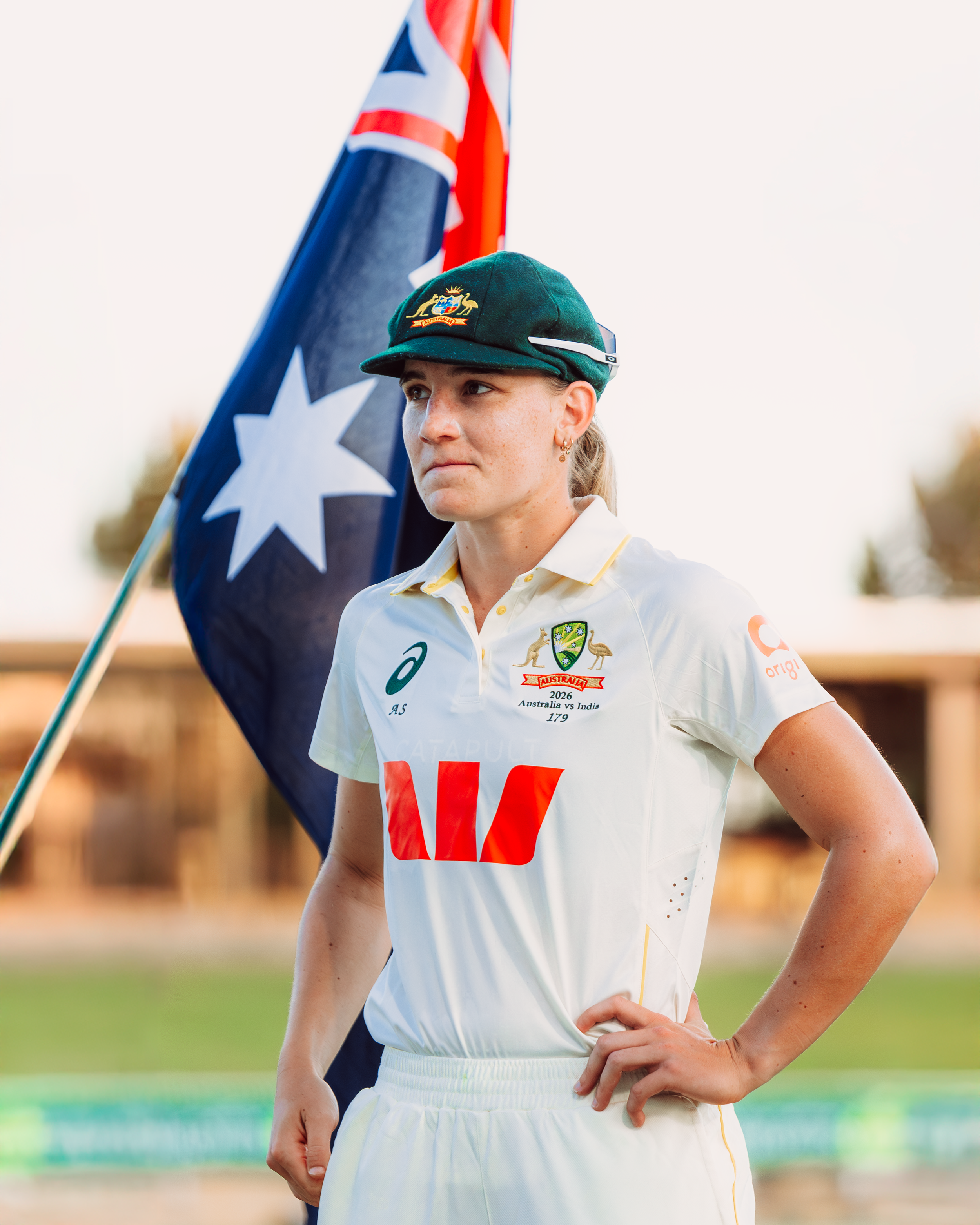 Australian female cricket player in uniform holding an Australian flag.