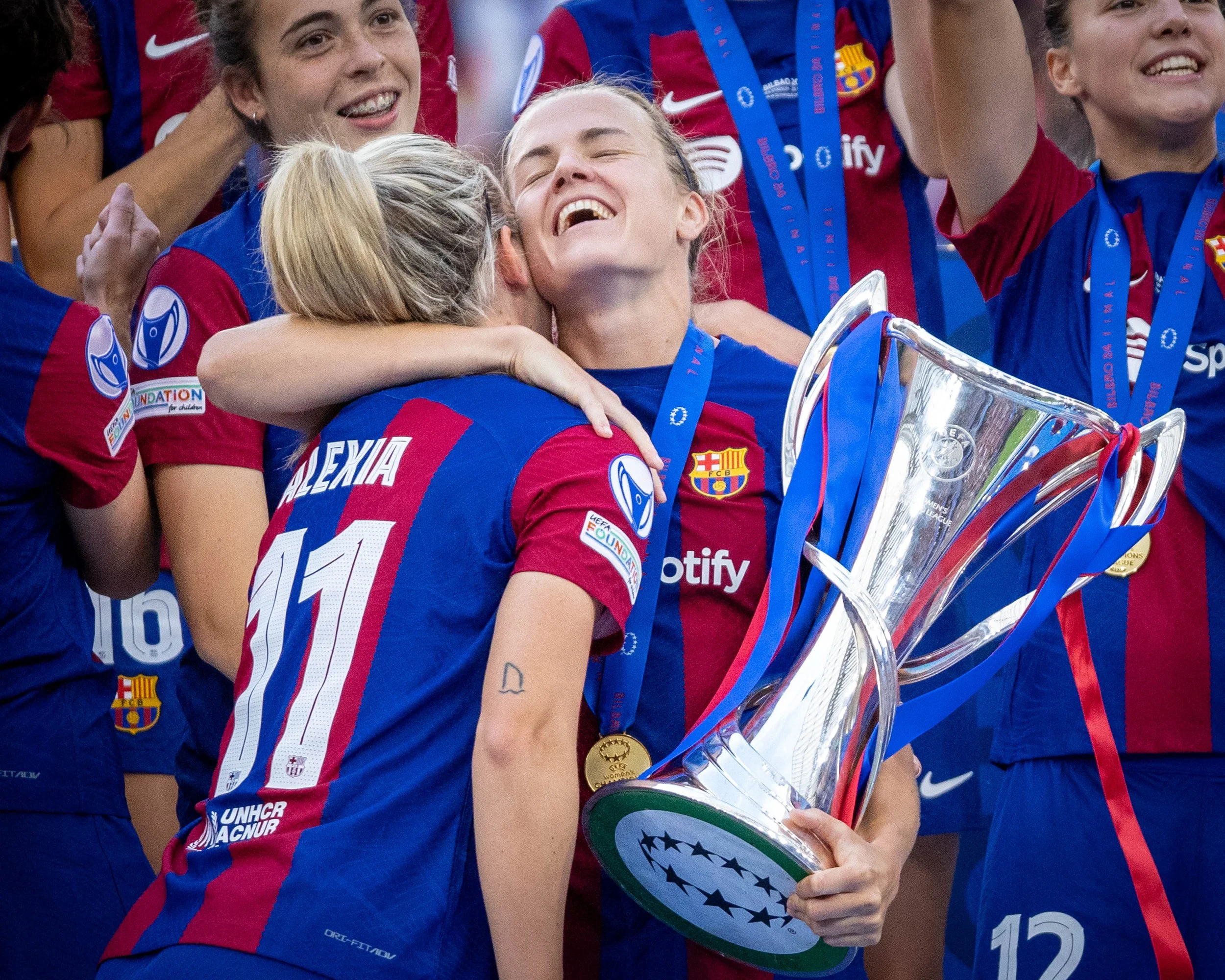 A group of female soccer players wearing FC Barcelona uniforms celebrating with medals and a trophy.