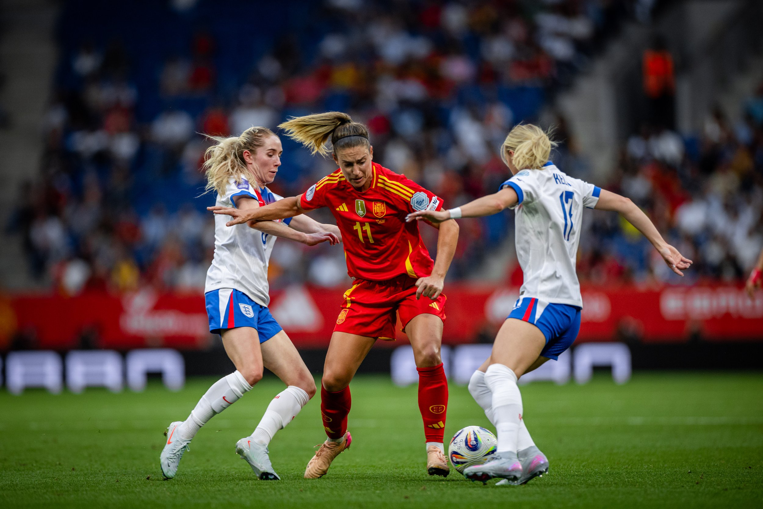 Women soccer players in white jerseys and one woman in a red jersey competing for the ball on the field during a match.