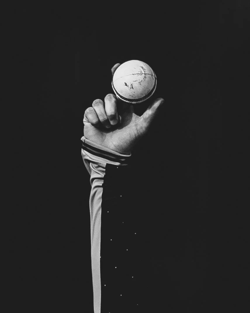 A person holding a well-worn baseball in their hand, with part of their attire visible, against a plain dark background.