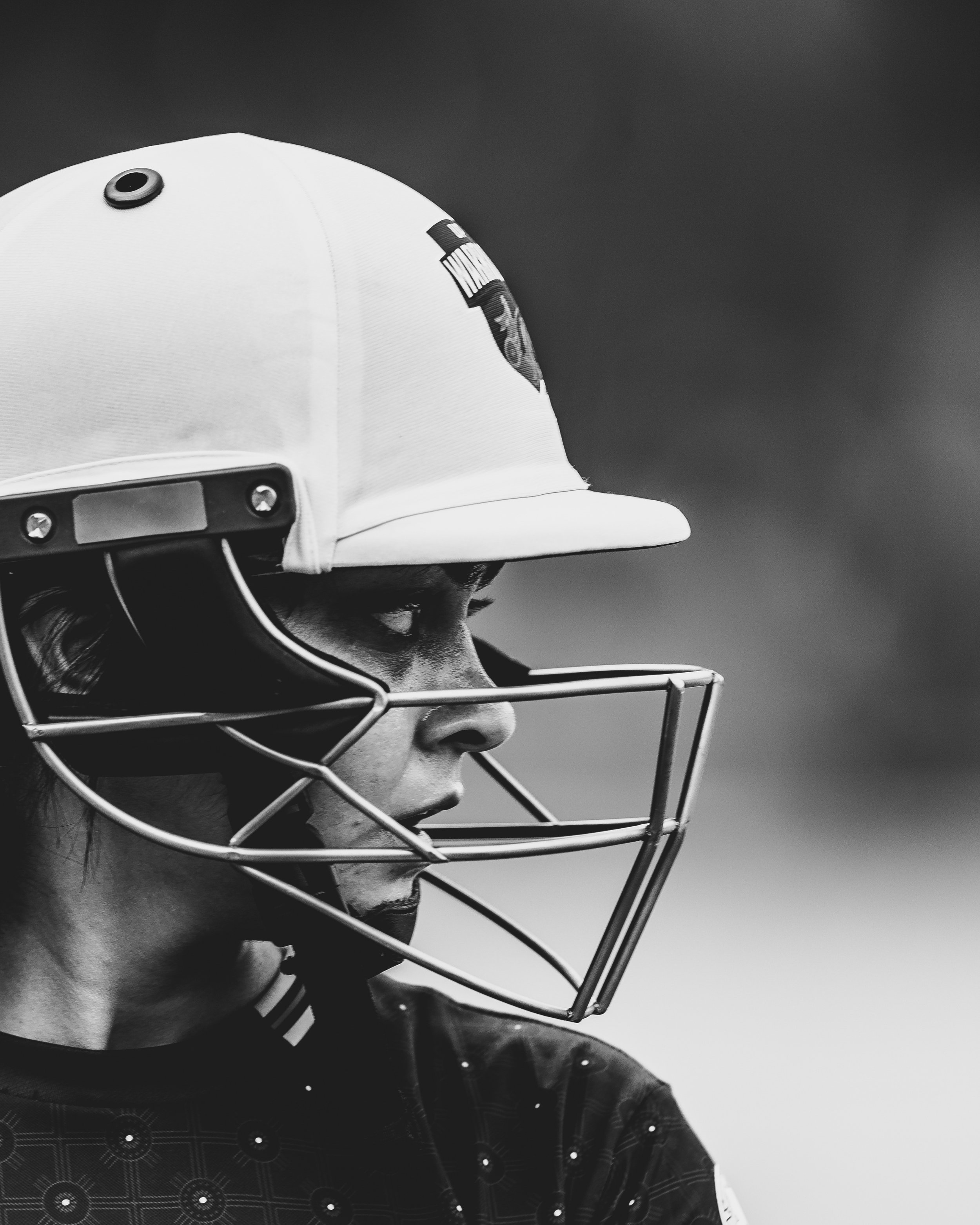 A black and white photo of a person wearing a white helmet and a face shield, with their head turned to the side, against a plain background.