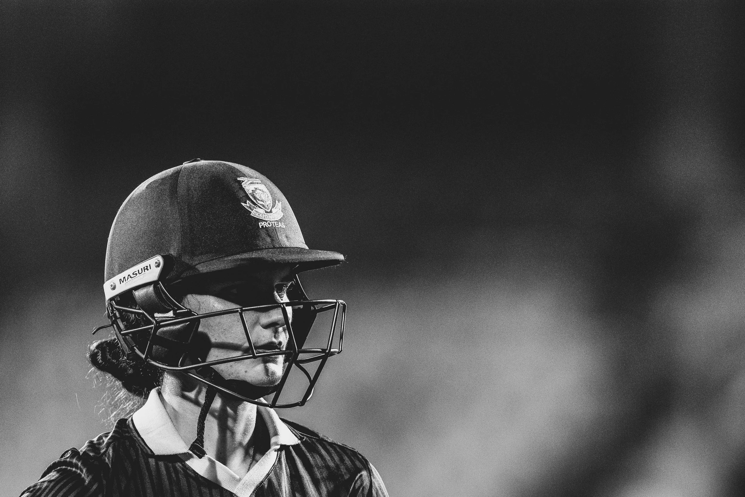 A woman wearing a football helmet and jersey, standing outdoors against a dark sky.