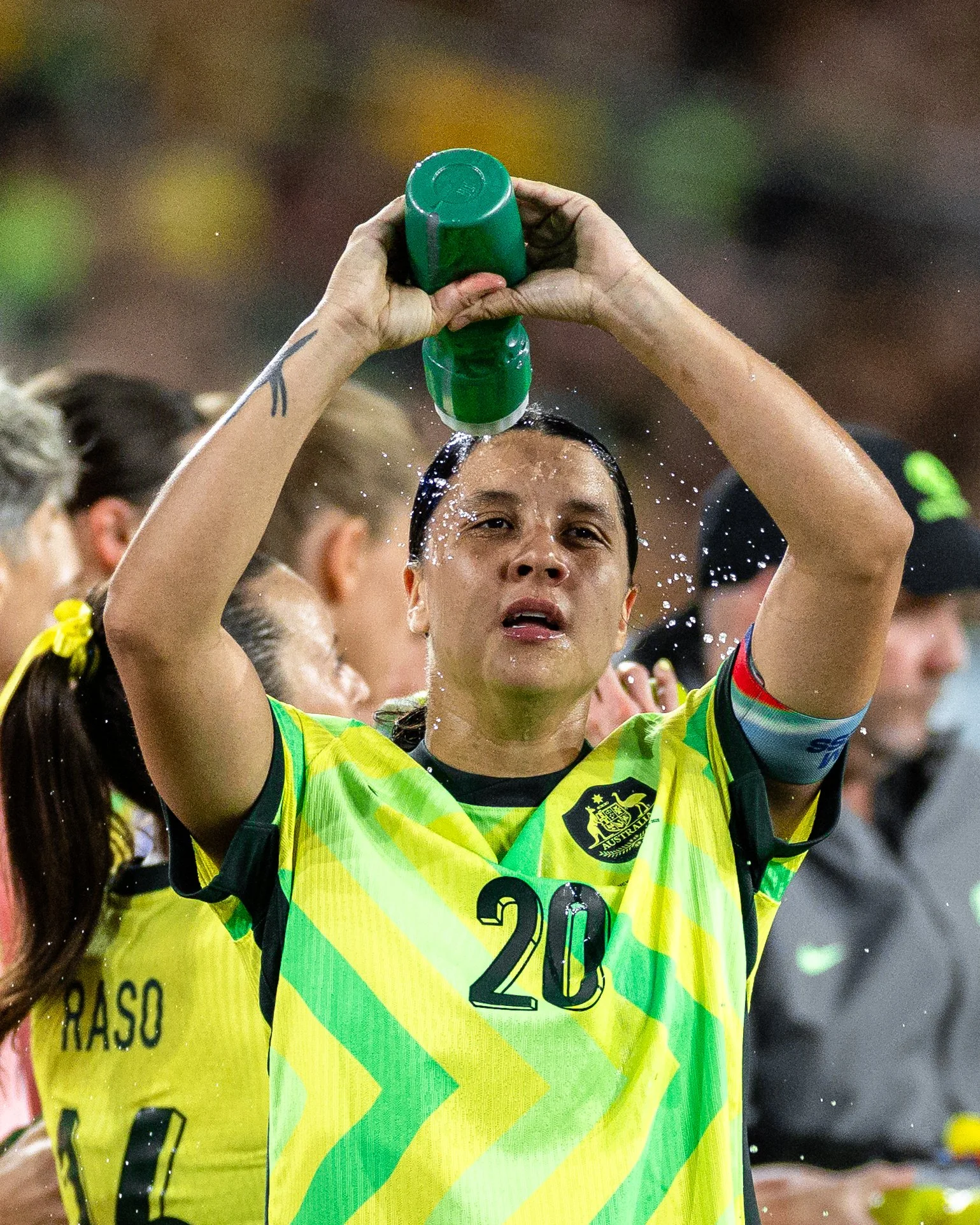 A person wearing a yellow and green sports jersey with the number 20, pouring water over their head during a celebratory moment at a sports event.