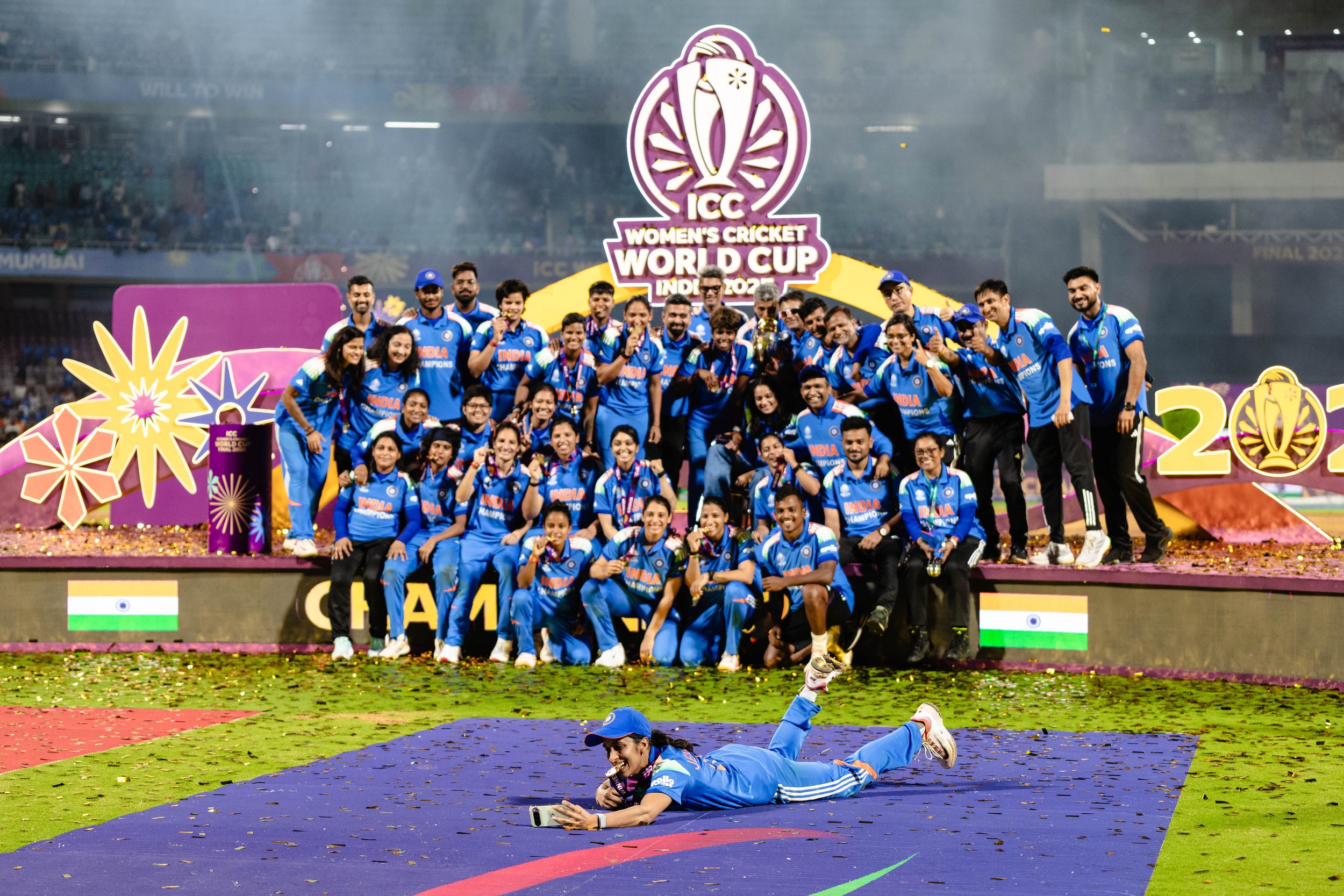 Indian women's cricket team celebrating their victory at the ICC Women's Cricket World Cup 2023, with team members smiling and holding medals, on a decorated cricket field with confetti and colorful banners.