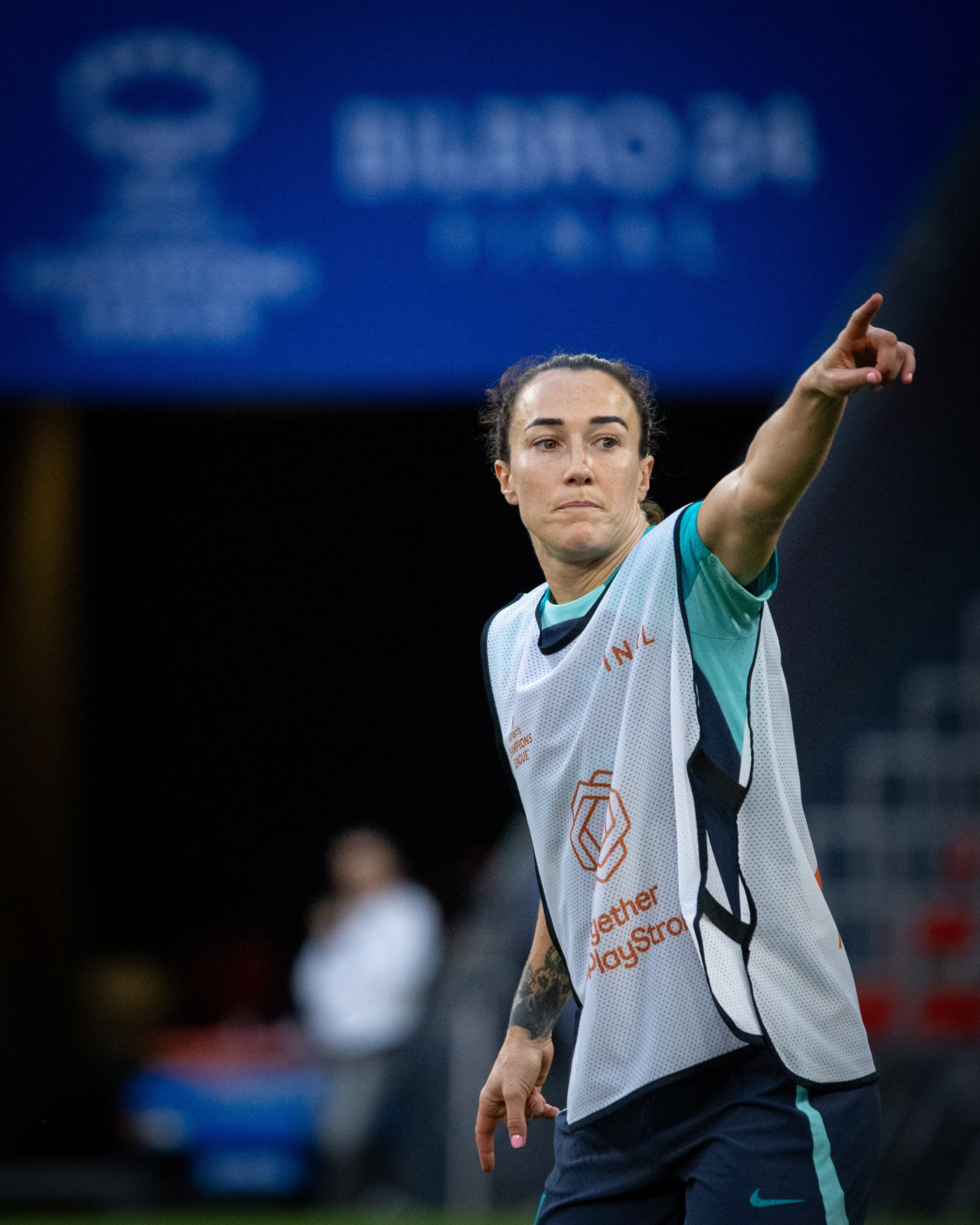 A female soccer player in a white and teal uniform points with her right hand during a game.