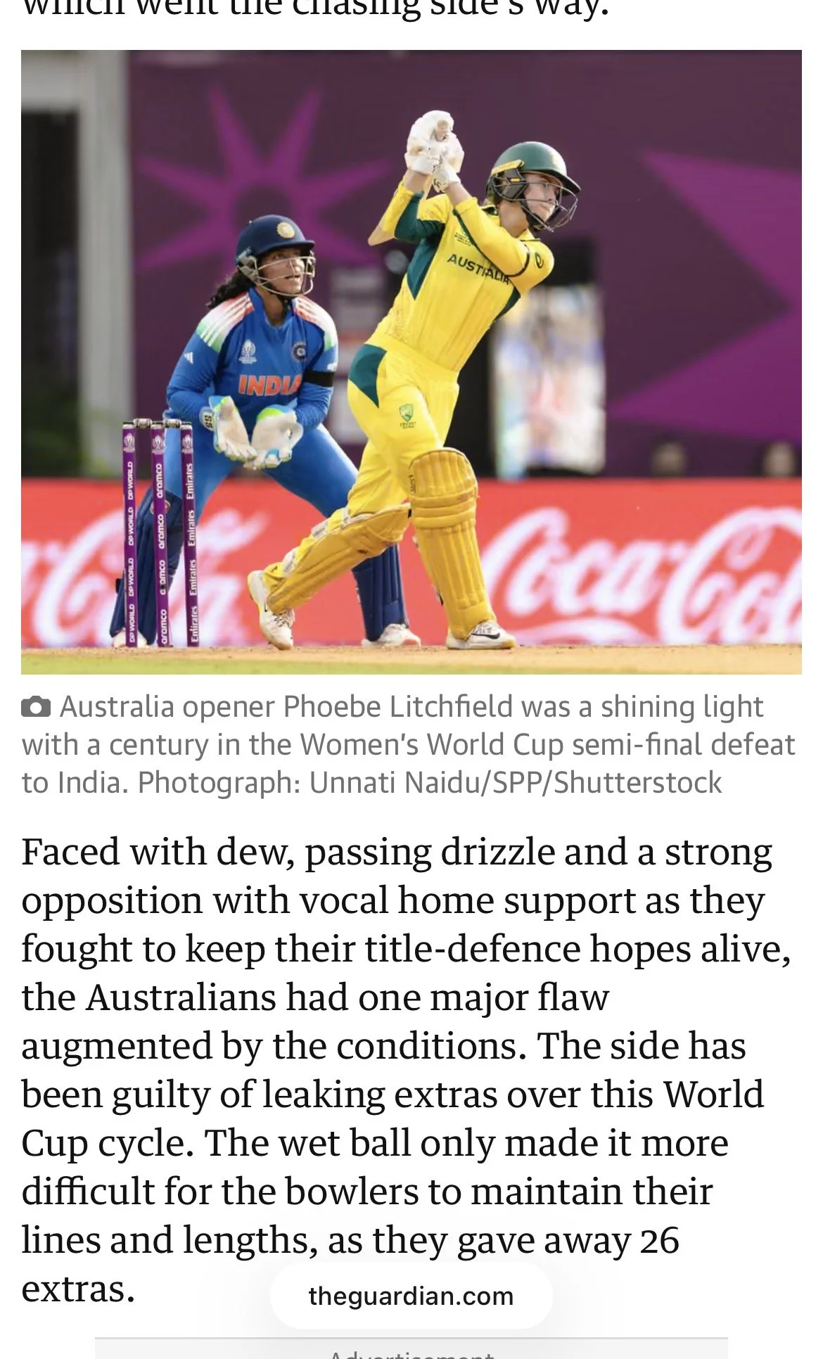 An Australian woman cricket player in yellow uniform swinging a bat during a match, with an Indian wicketkeeper behind her, a purple background, and a Coca-Cola advertisement along the boundary.