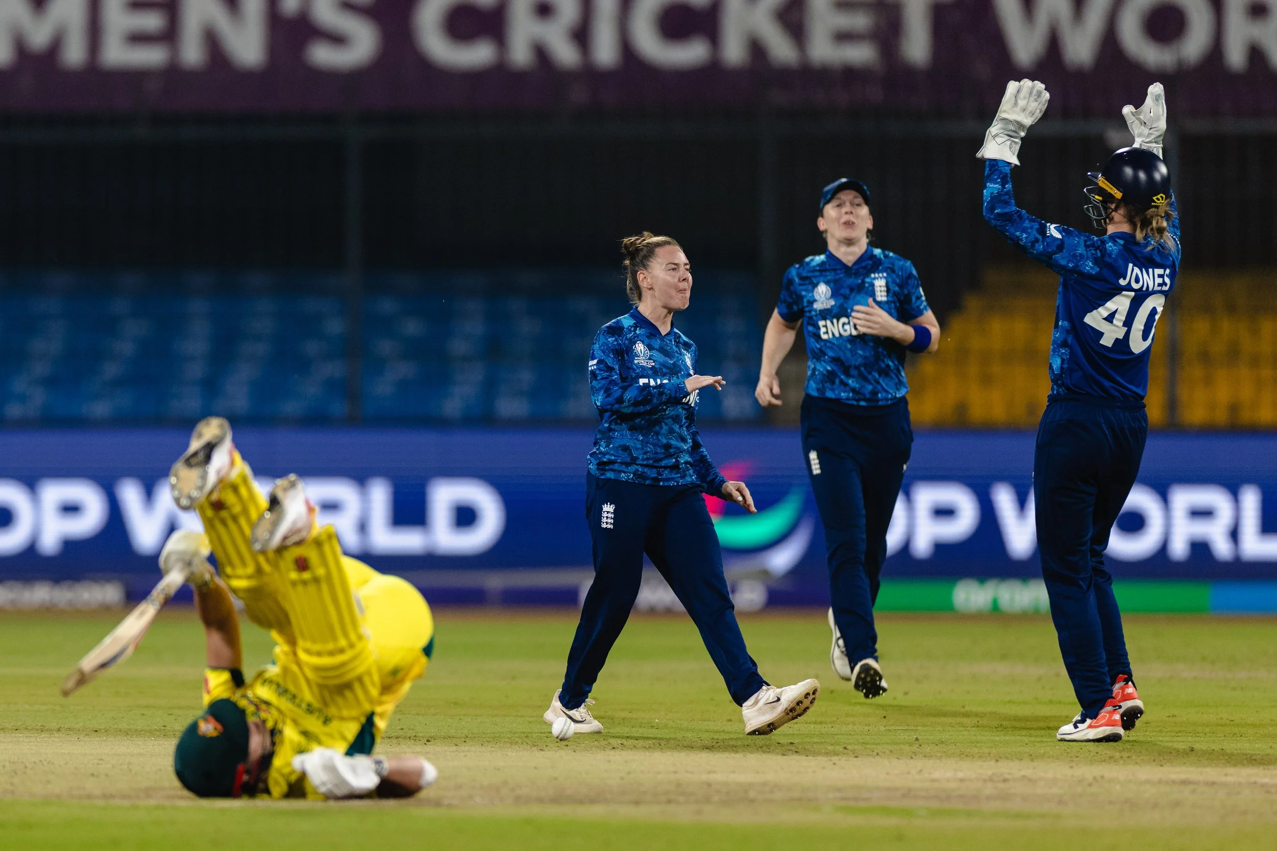 England women's cricket team players celebrating on the field while an injured player lies on the ground during a match.