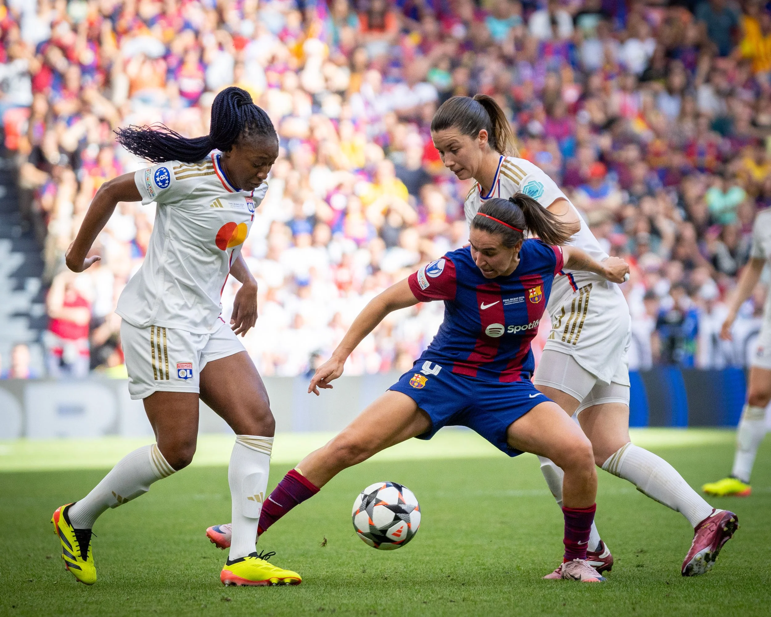 Women playing soccer during a match with a crowd in the background.