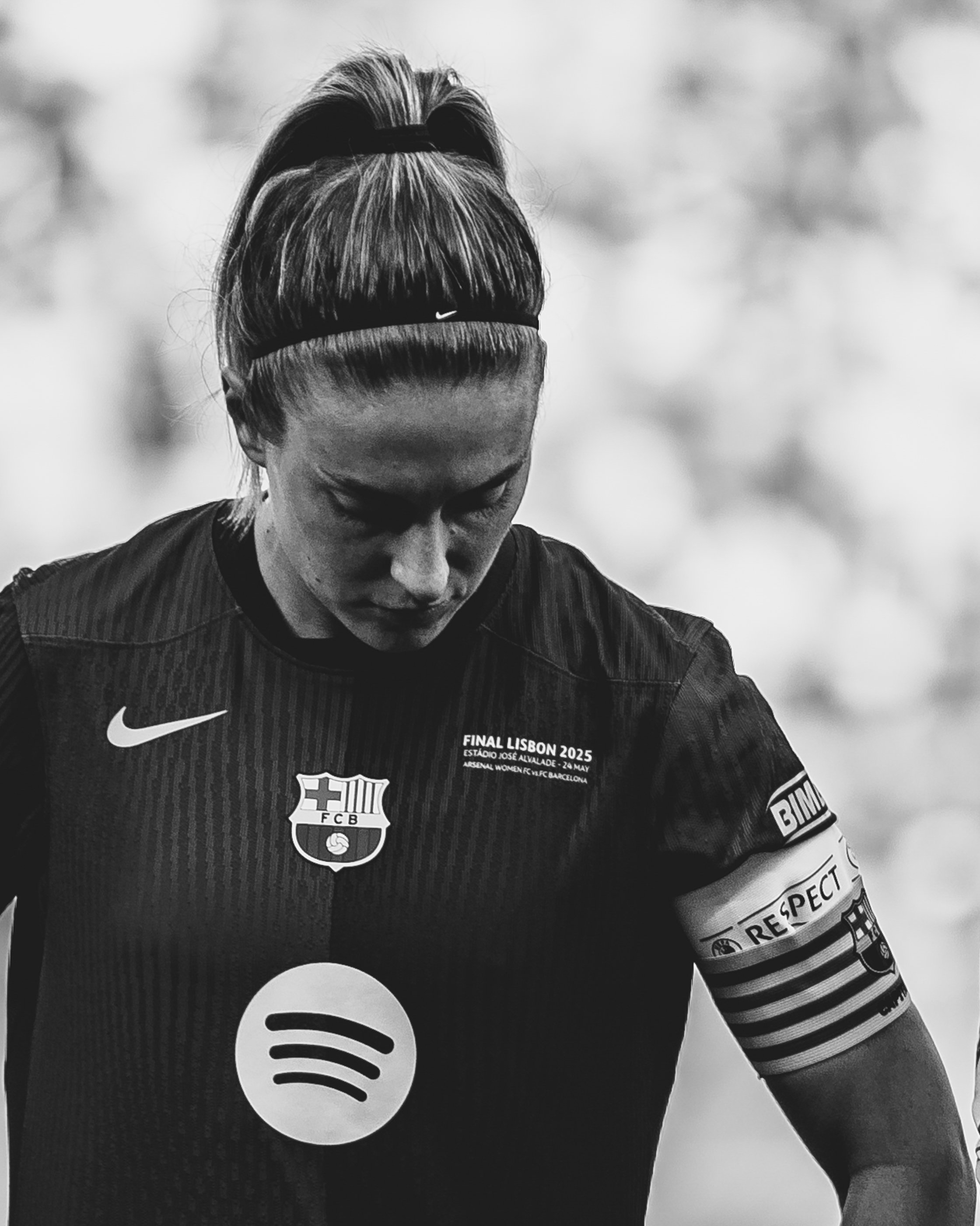 Close-up black and white image of a female athlete wearing a Barcelona football jersey, with her head bowed down, a Nike sports headband, and the Spotify logo on her shirt. The jersey reads "Final Lisbon 2025," and various sponsor patches are visible