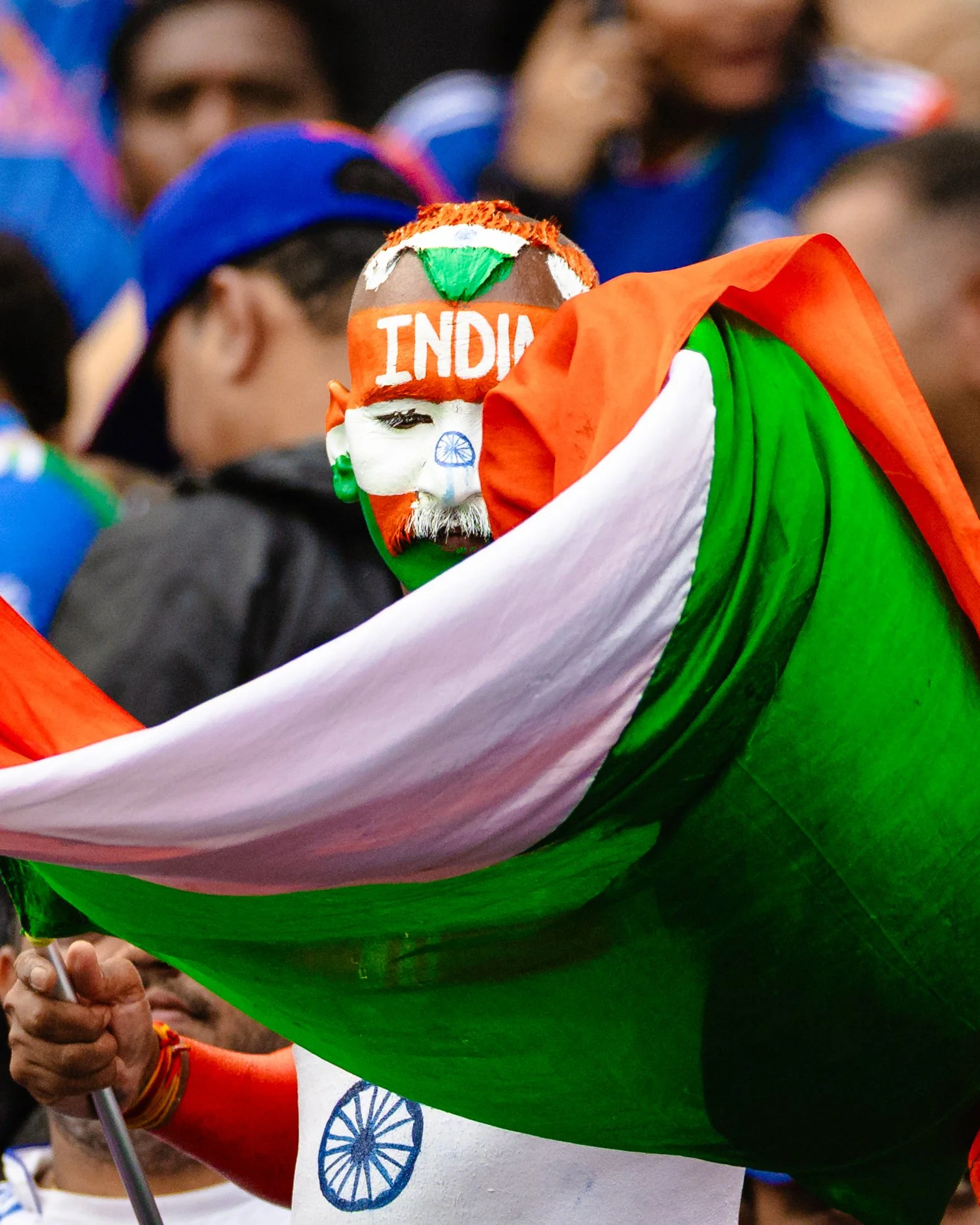 Person wearing a face mask painted with the Indian flag colors, with 'INDIA' written on it, holding an Indian flag draped over their shoulder, celebrating a patriotic event.