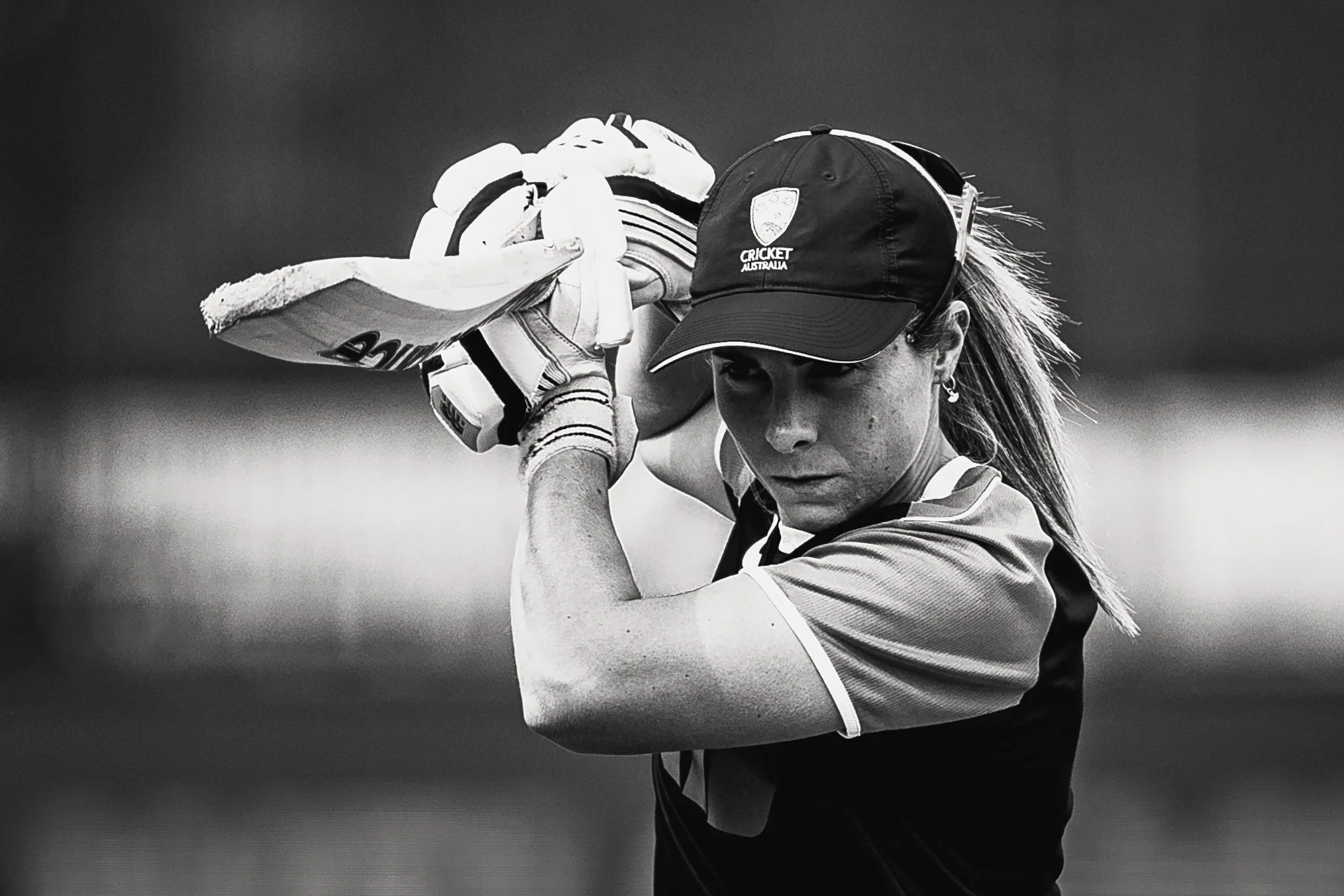 A female cricket player wearing a cap with the words 'Cricket Australia' is preparing to bat with a cricket bat, focusing on her action.