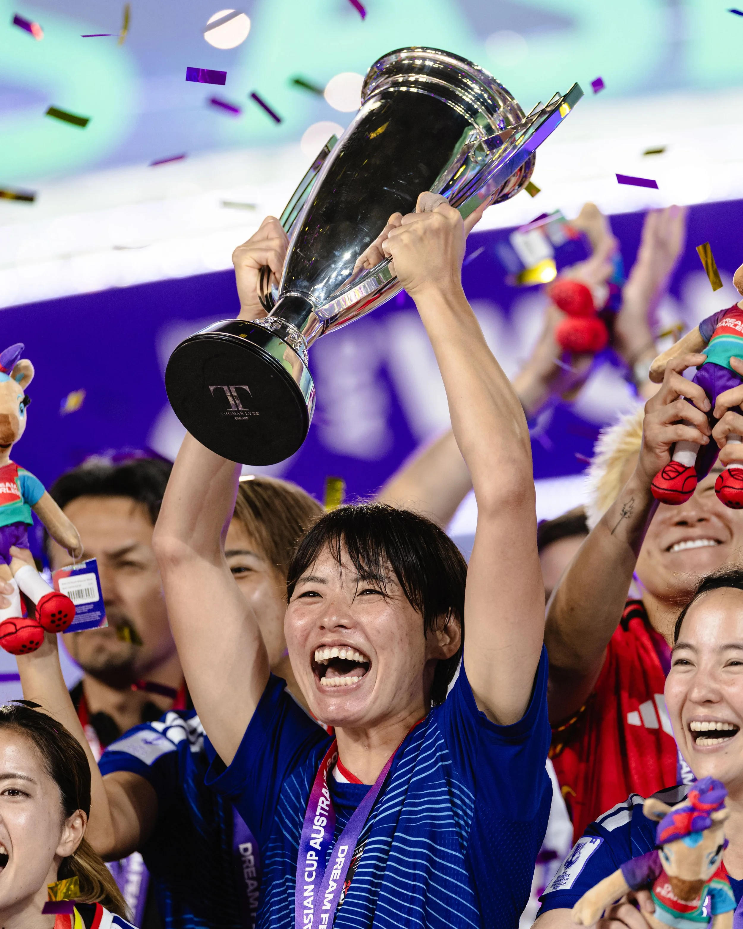 A person celebrating with a trophy, surrounded by confetti and other people, at a sports event.