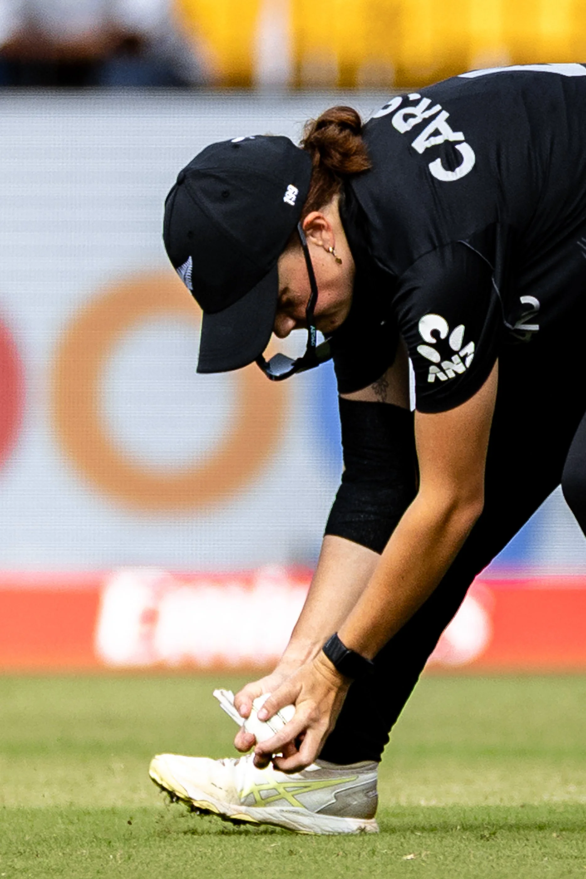 A woman in a black sports uniform is positioning to kick a white ball on a grass field during a sports event.