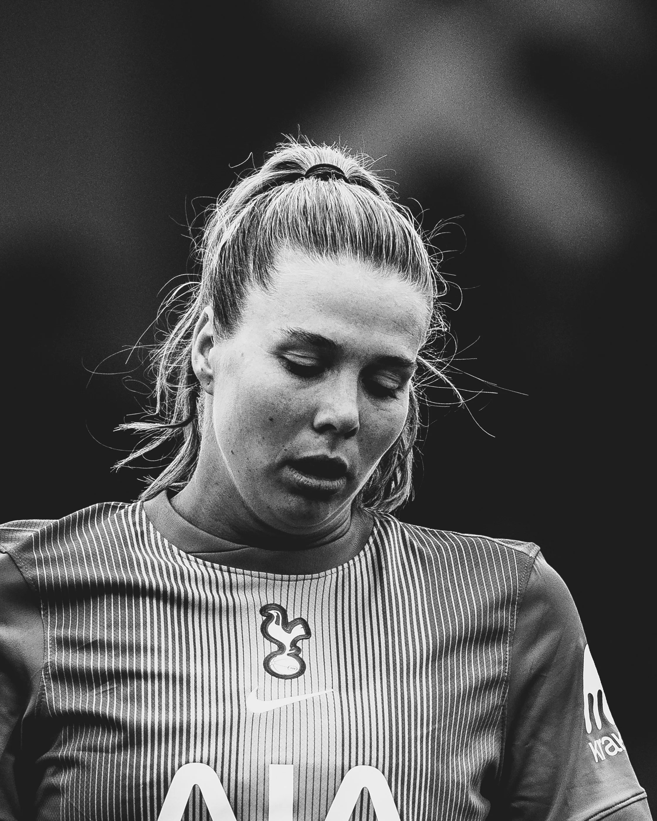 Close-up of a female athlete wearing a striped sports jersey with a question mark necklace, looking down with a serious expression.