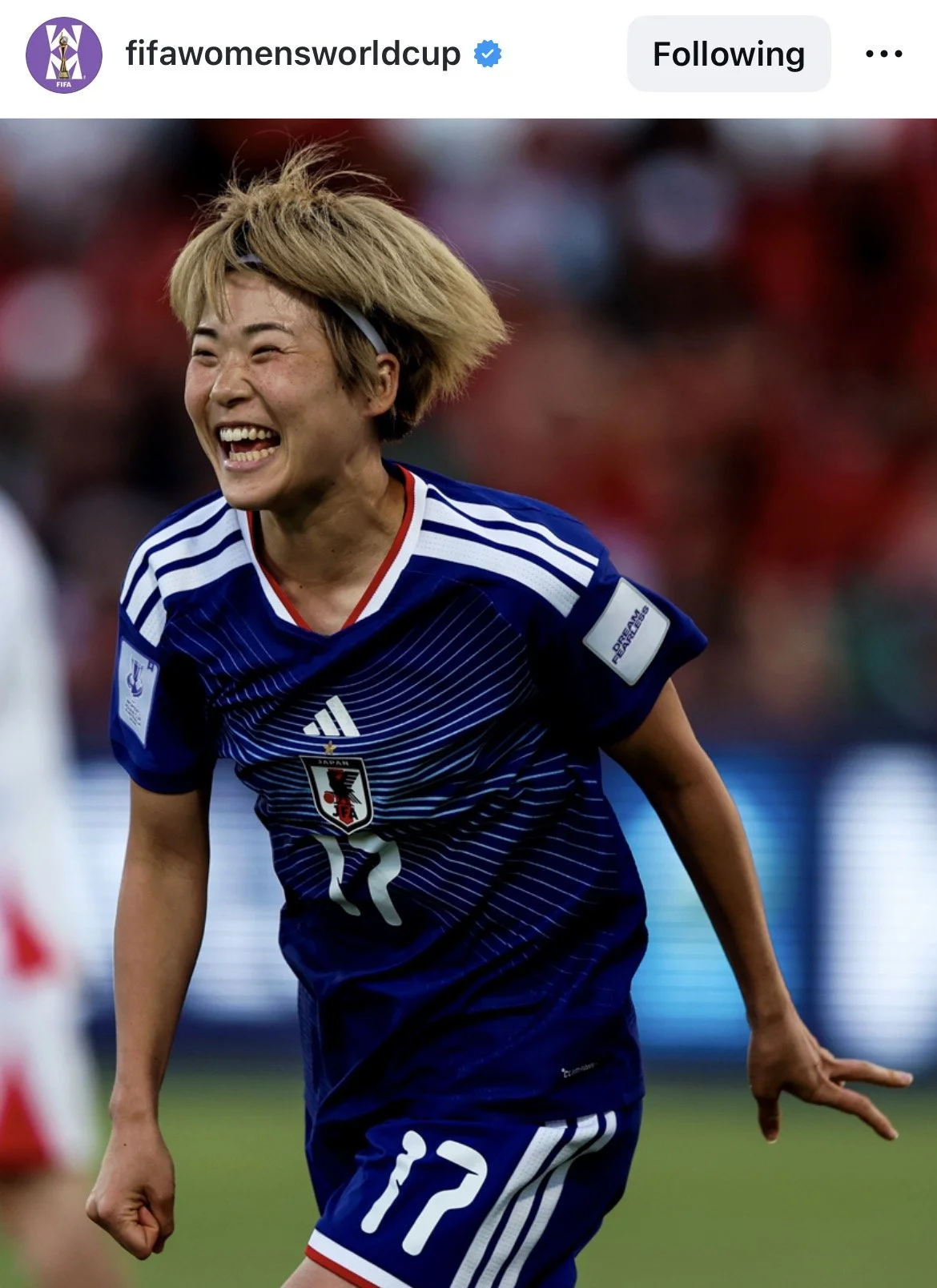 A woman in a Japan soccer jersey celebrating with a big smile, celebrating a victory or a goal on the soccer field.