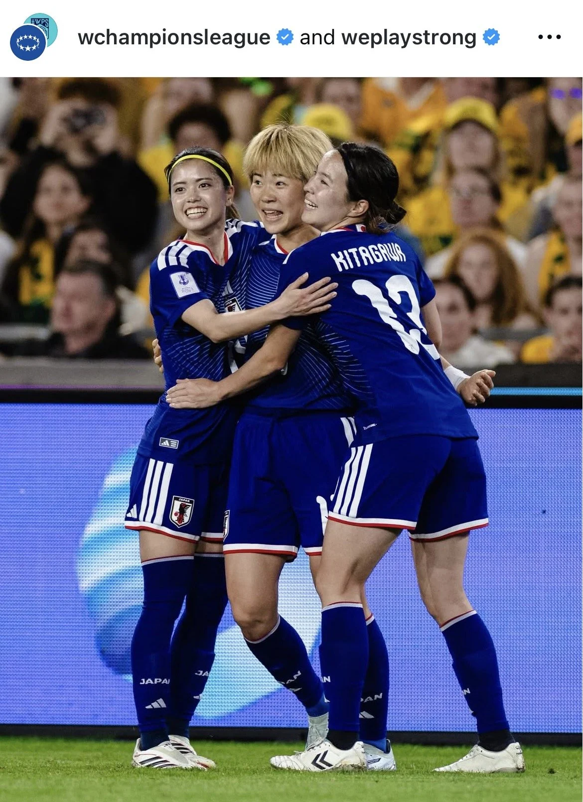 Japanese women's soccer team celebrating together on the field during a match, wearing blue jerseys with Japan's emblem.