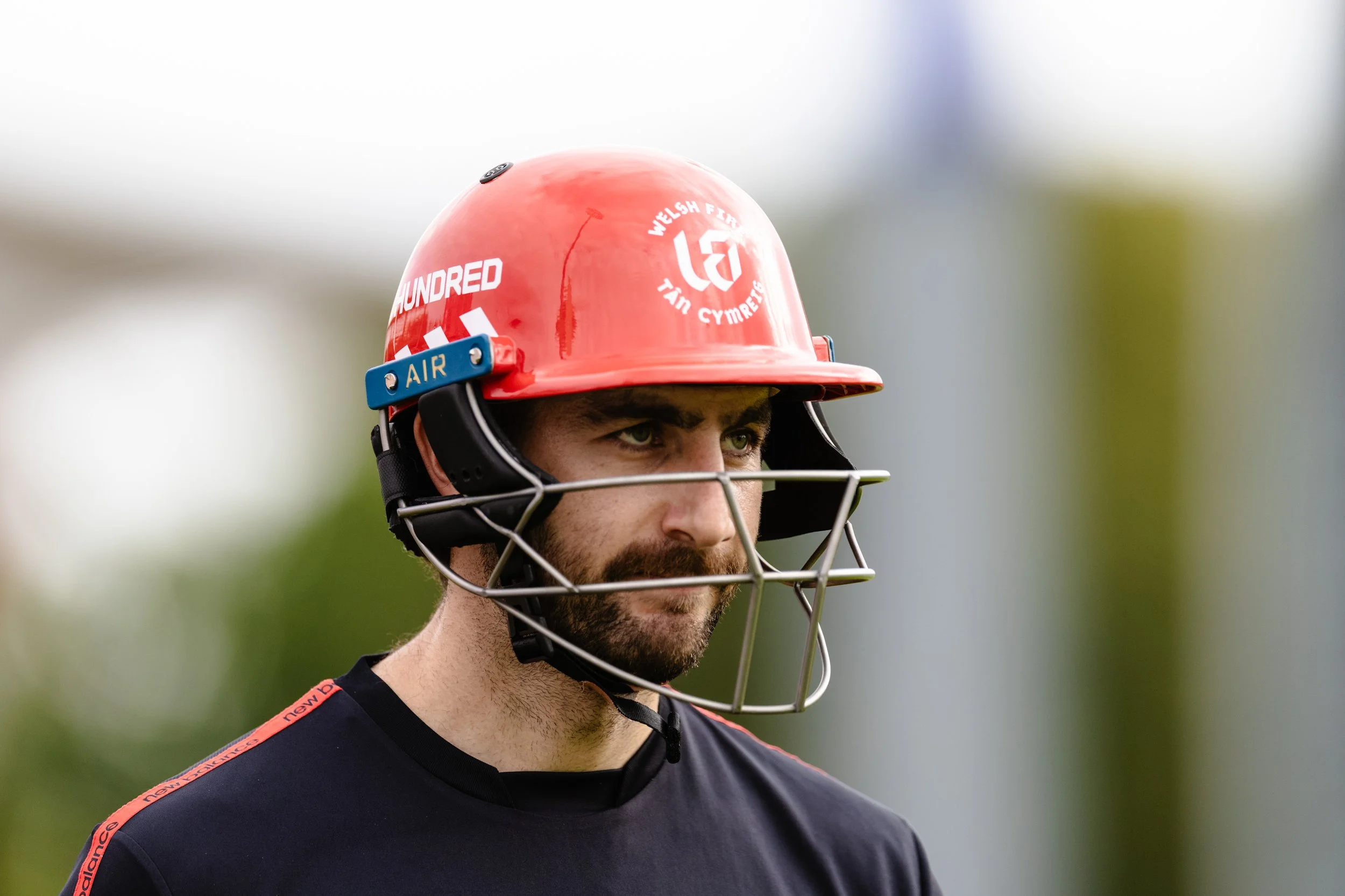 A young man wearing a red firefighter helmet with white writing and a black face mask hanging around his neck.