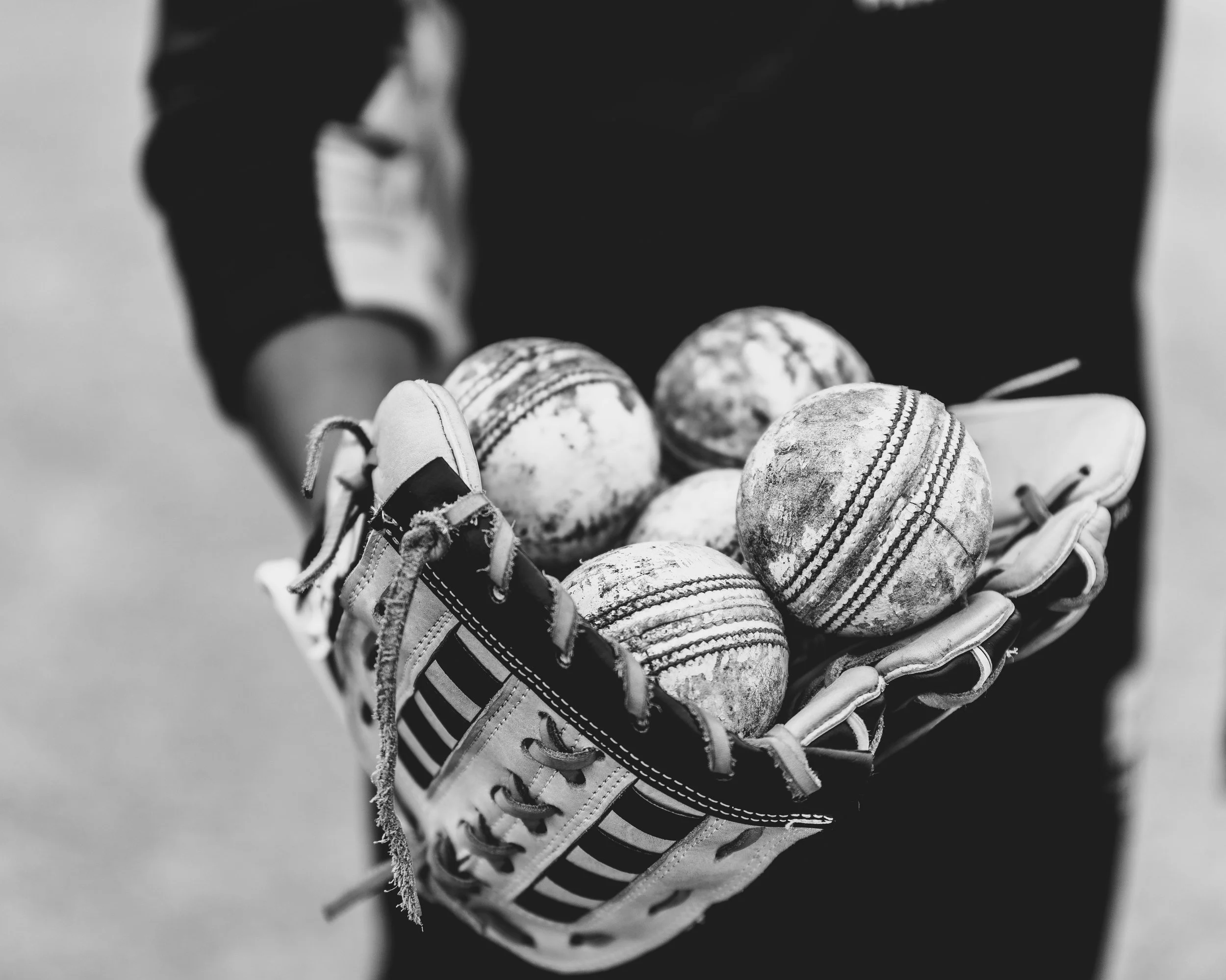 Black and white photograph of a pair of worn baseball cleats with dirt marks, placed in an open sports glove, against a blurred dark background.