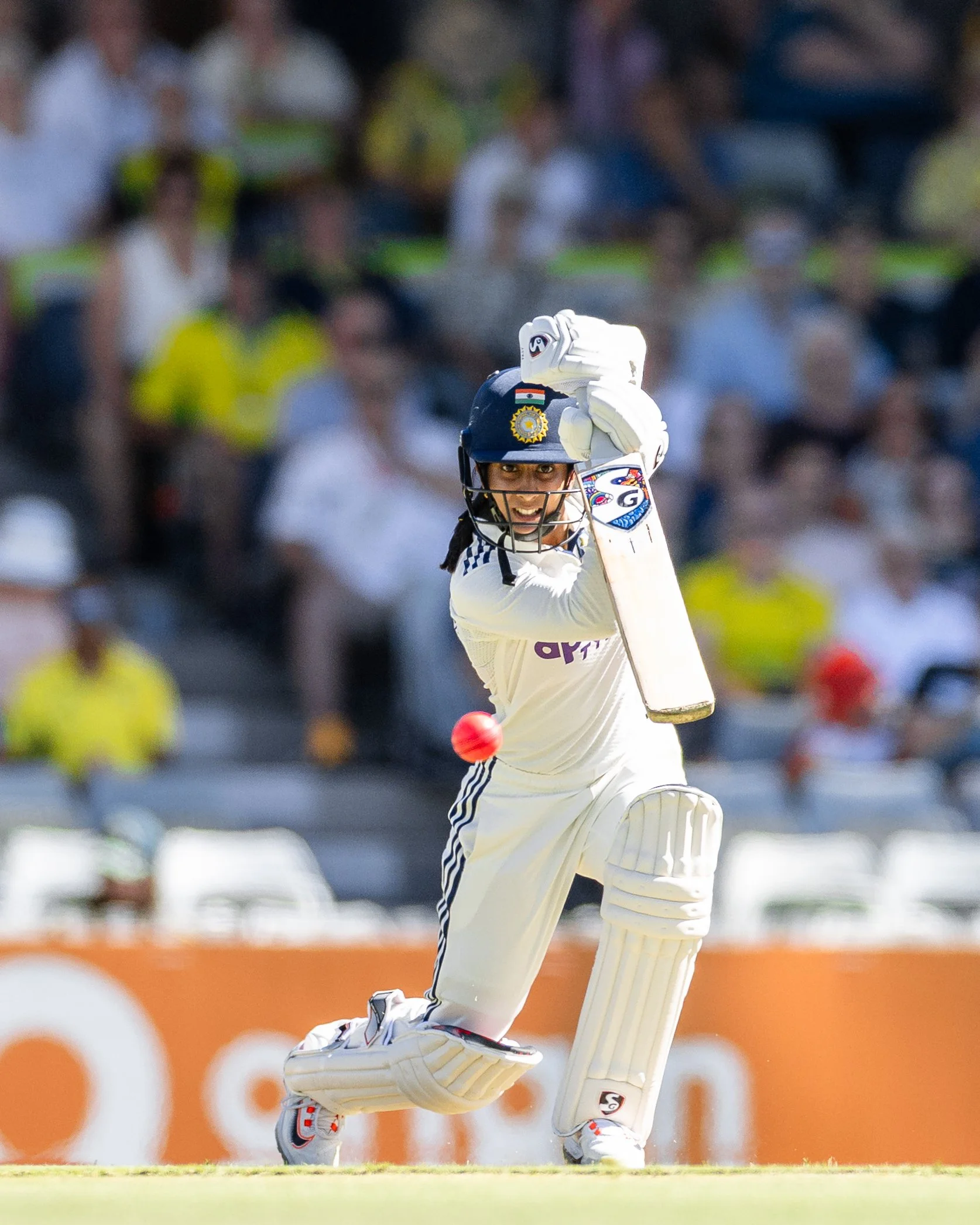 An Indian cricket player in white uniform and a dark blue helmet is sliding on the ground while celebrating a wicket during a cricket match on a cricket field, with a crowd of spectators in the background.