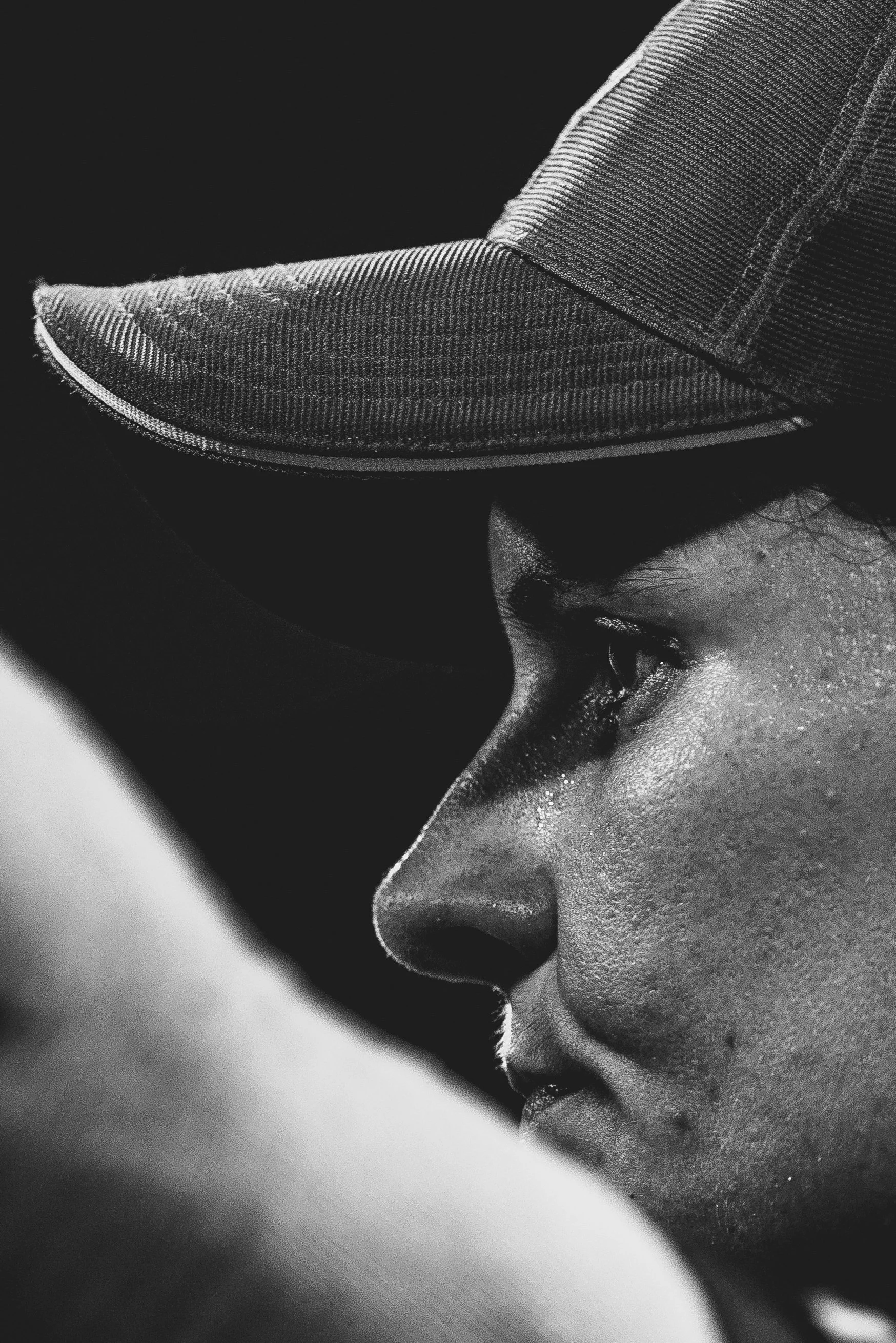 Close-up black-and-white photo of a person wearing a baseball cap, with the person's eyes closed and face resting on their arm.