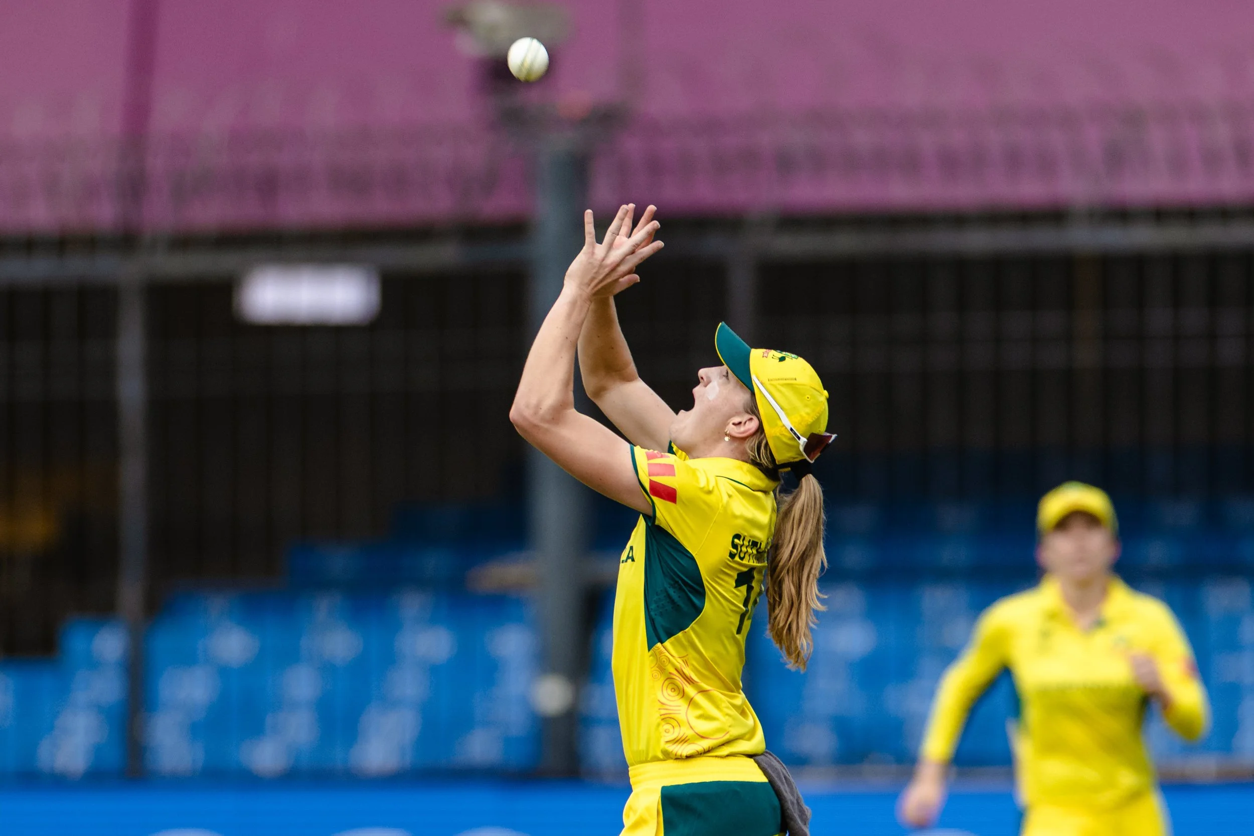 A female volleyball player in a yellow and green jersey and cap preparing to hit a volleyball on a court.