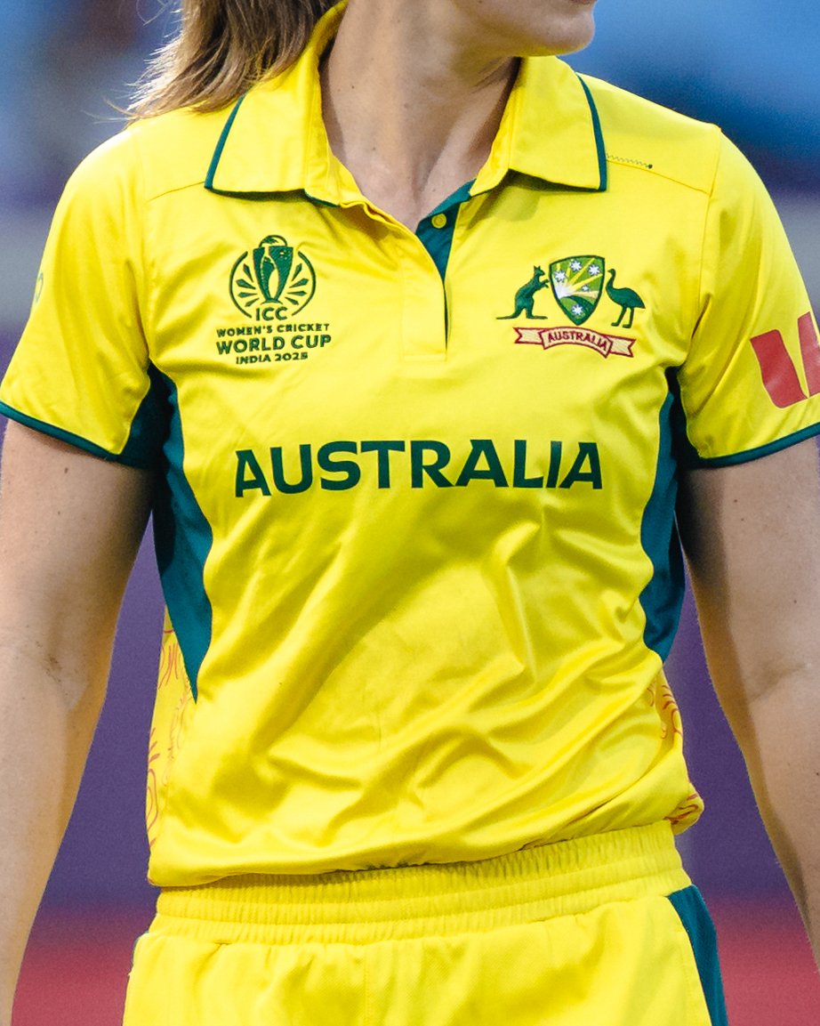 Close-up of a female cricket player wearing a yellow Australia team jersey with green accents, featuring logos and text including Women's Cricket World Cup 2023 and Australia.
