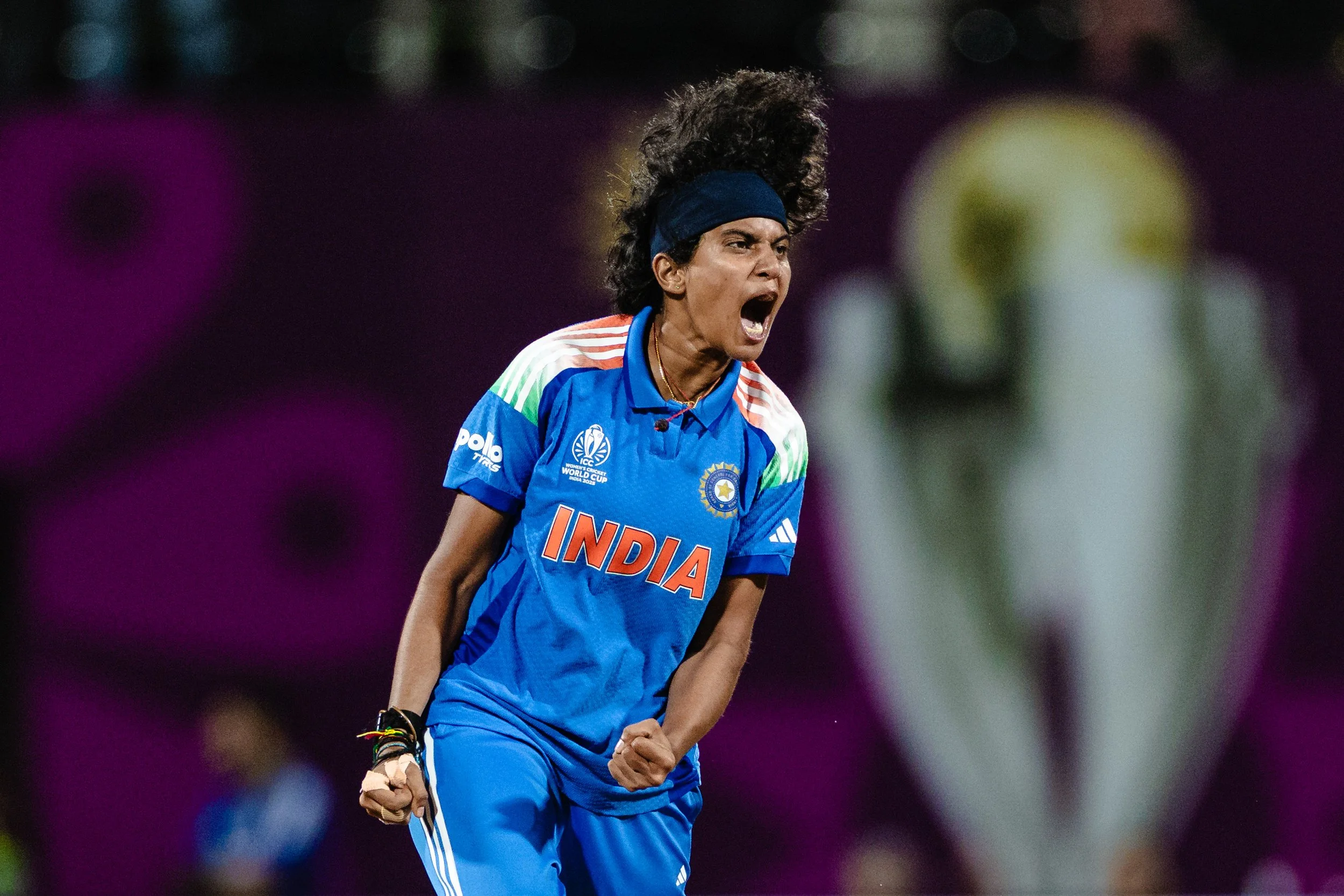 A female cricket player wearing the Indian national team uniform, celebrating with a fierce expression, her fist clenched, during a match.