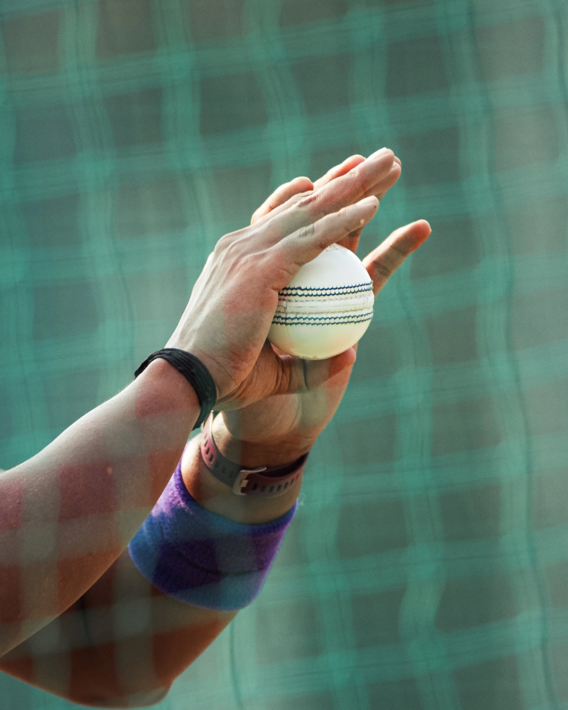 A hand holding a baseball over a green tennis court.