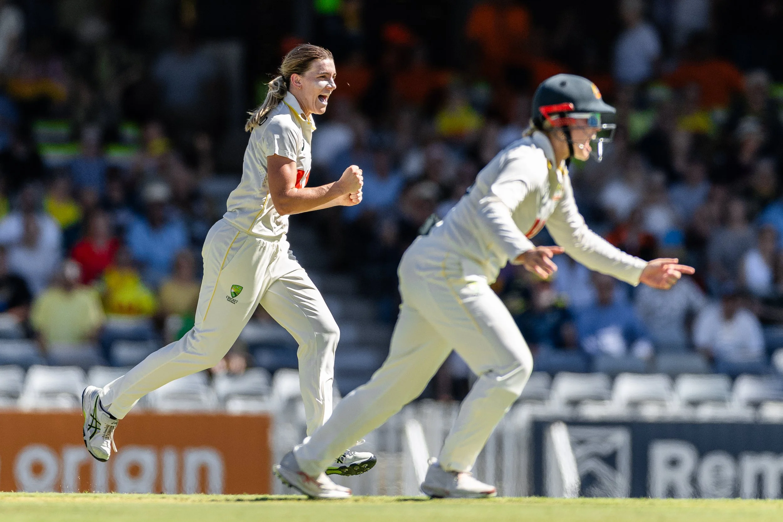 Cricket players running on the field during a match, with spectators in the background.